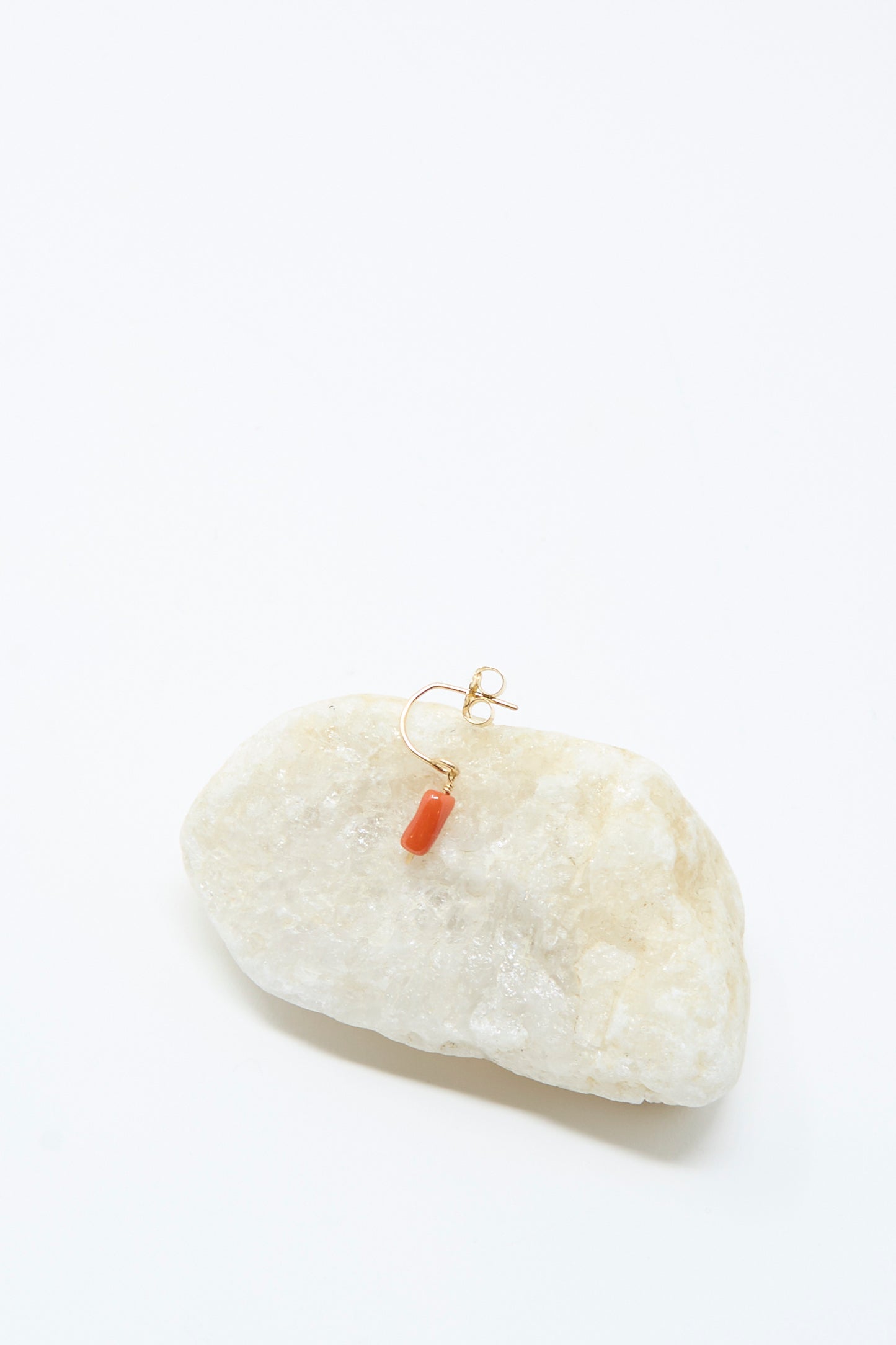 The Mary MacGill 14K Crescent Charm Single Earring in Coral Pebbles rests on a large white stone against a plain white background.