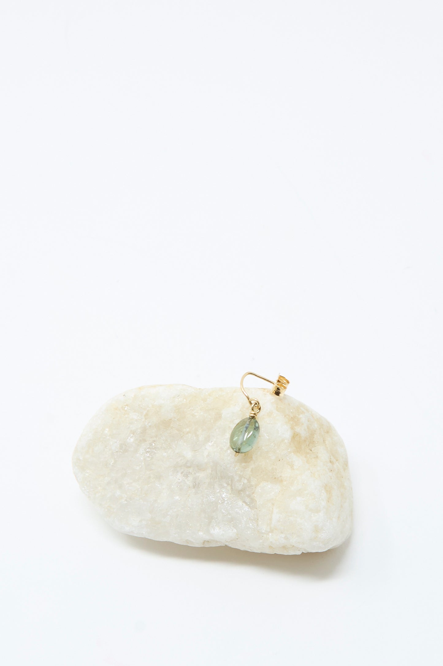 The Mary MacGill 14K Crescent Charm Single Earring in Round Tourmaline features a handmade gold design with a small green gemstone, shown dangling from a light-colored stone on a plain white background.