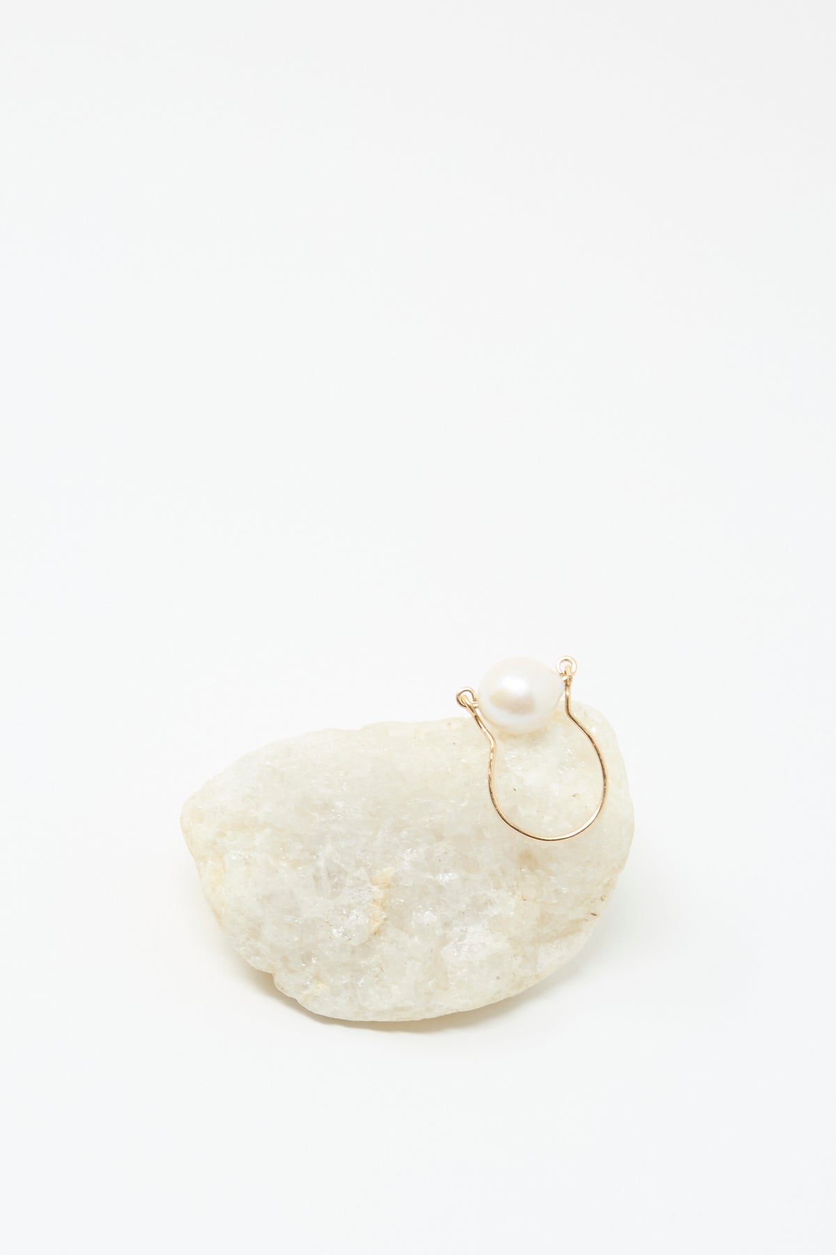 The Baroque Pearl Ring in White by Mary MacGill, featuring a single white pearl on gold-filled wire, is displayed on a rough white stone against a plain white background.