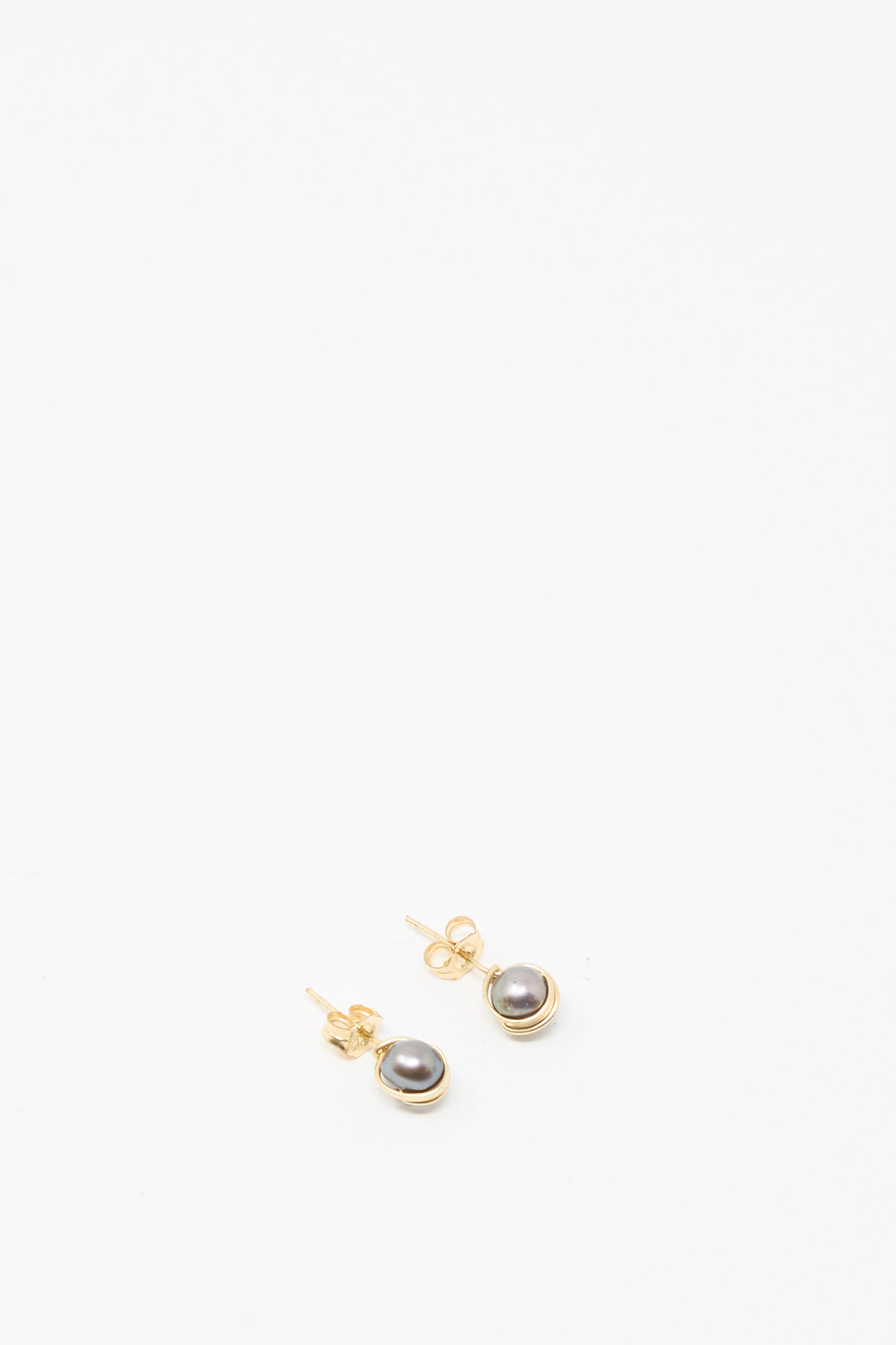 The Baroque Pearl Studs in Charcoal by Mary MacGill are small gold-filled earrings with dark round pearls, shown on a plain white background.