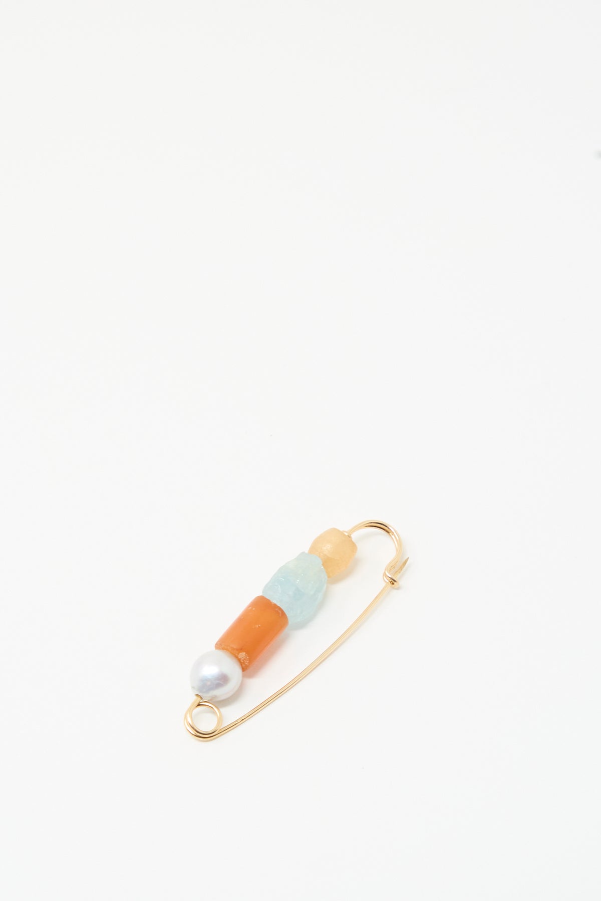 The Rising Summer Pin by Mary MacGill features four beads—baroque pearl, orange carnelian, blue, and beige—handmade on a gold safety pin.