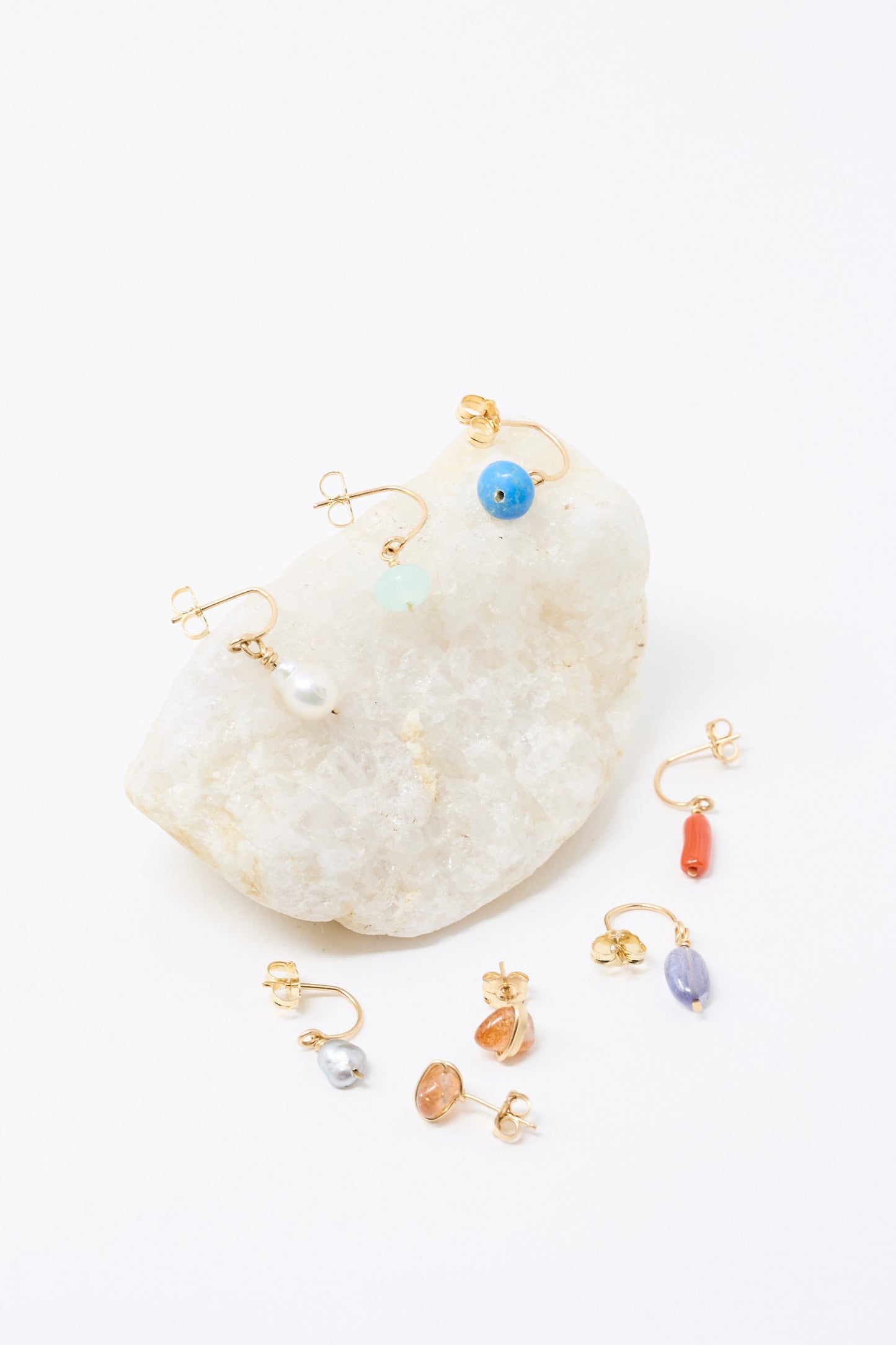 Mary MacGill's Stone Studs in Sunstone, made with gold-filled wire are displayed with other earrings on a white stone against a white background.
