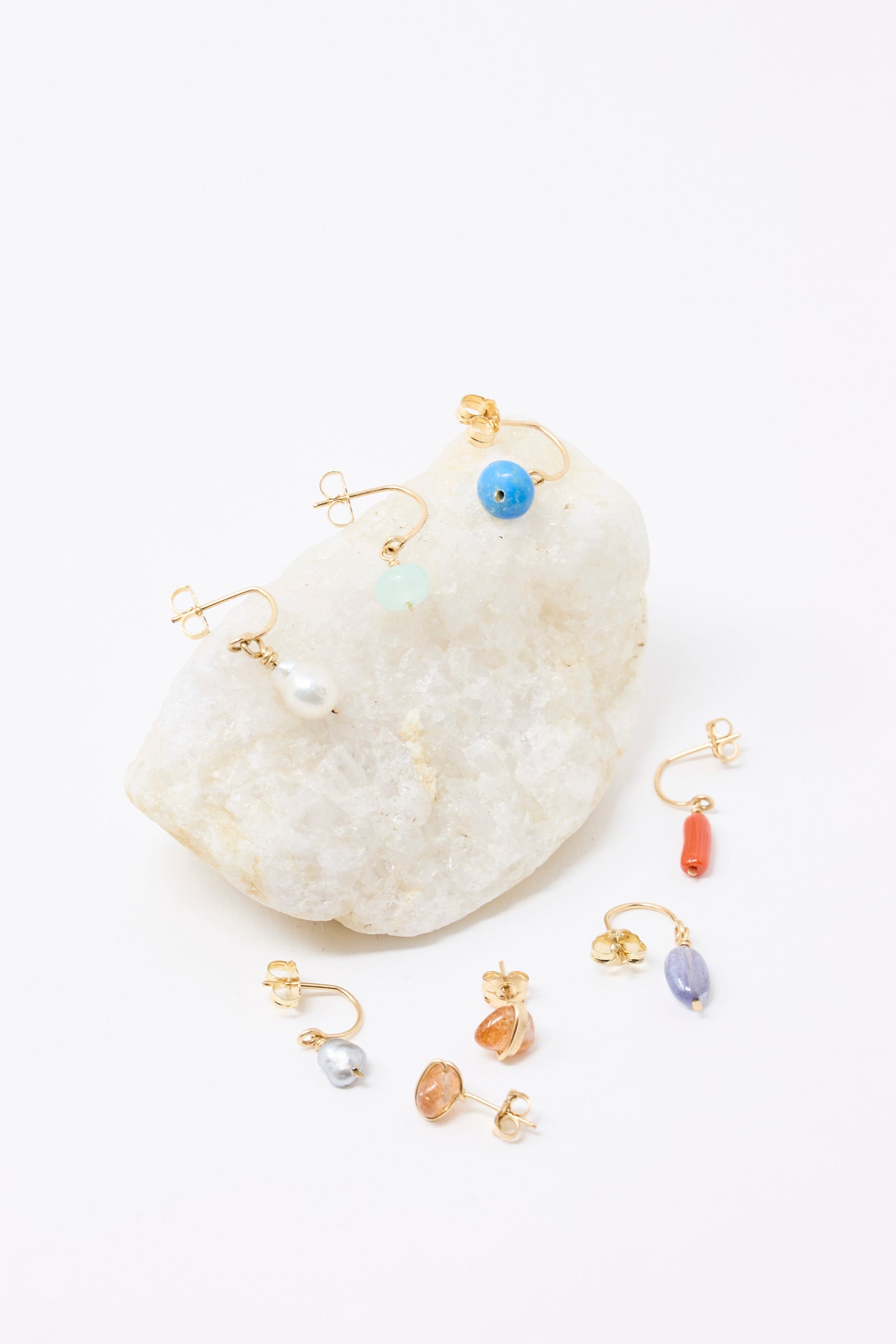 Mary MacGill's Stone Studs in Sunstone, made with gold-filled wire are displayed with other earrings on a white stone against a white background.