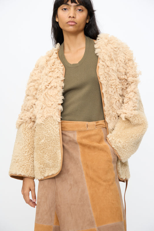 A woman stands against a plain white background wearing Milena Silvano's Pyramid Robe in Oat, styled with an olive green top and a tan patchwork suede skirt made in Turkey.
