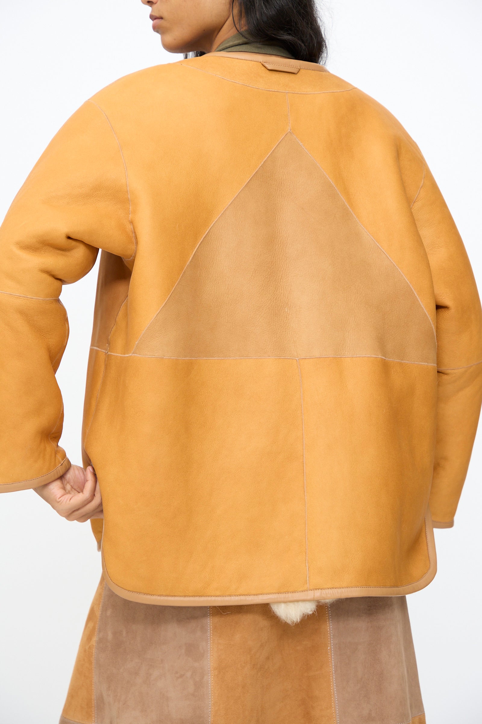 A person wearing the Milena Silvano Pyramid Robe in Oat, a tan and camel patchwork sheepskin coat made in Turkey, is photographed from the back against a plain white background.