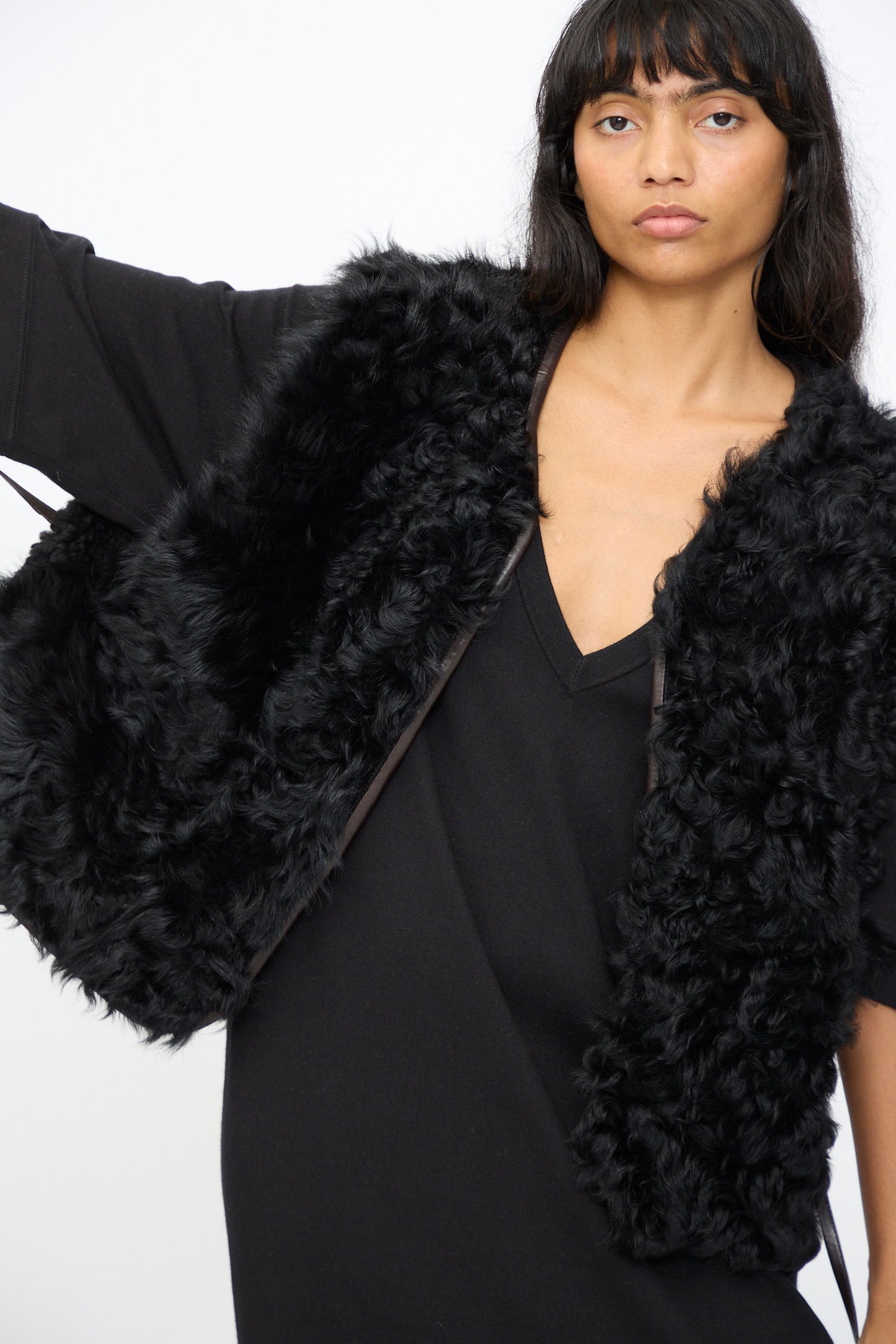 A woman in a black V-neck dress and a relaxed fit vest stands against a white background. She wears the Milena Silvano Transition Vest in Chaga, a textured black vest.