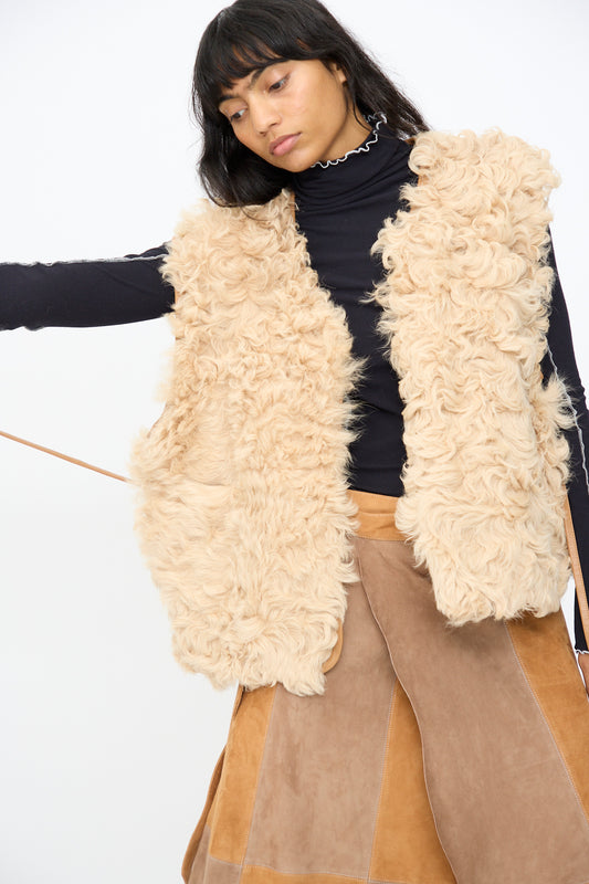A person wears the Milena Silvano Transition Vest in Oat over a black turtleneck and a brown patchwork skirt, standing against a plain white background.