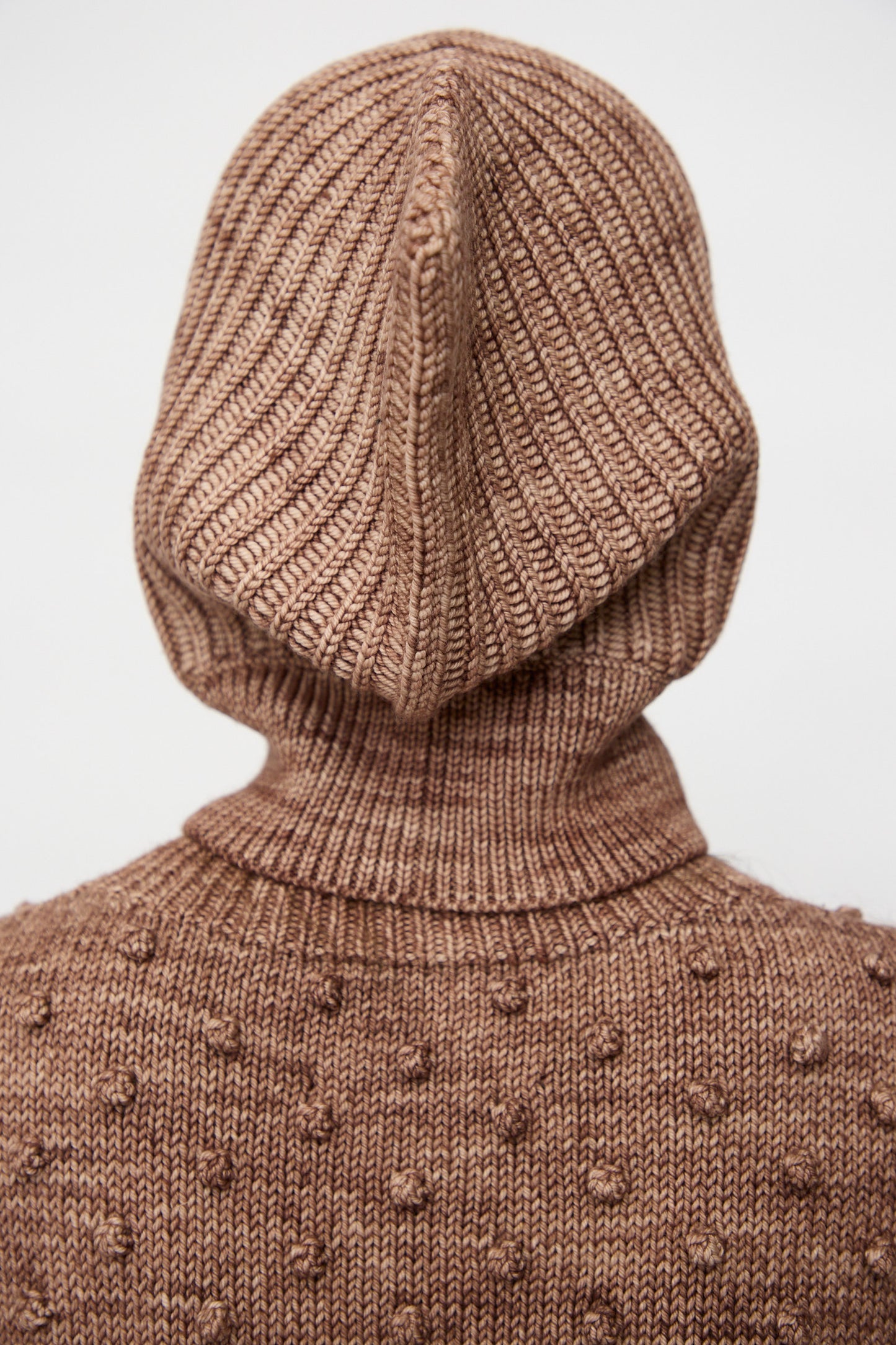 A person is seen from the back wearing the Misha & Puff Fisherman Hood in Affogato, a brown textured sweater with a merino cashmere hood, set against a plain background.