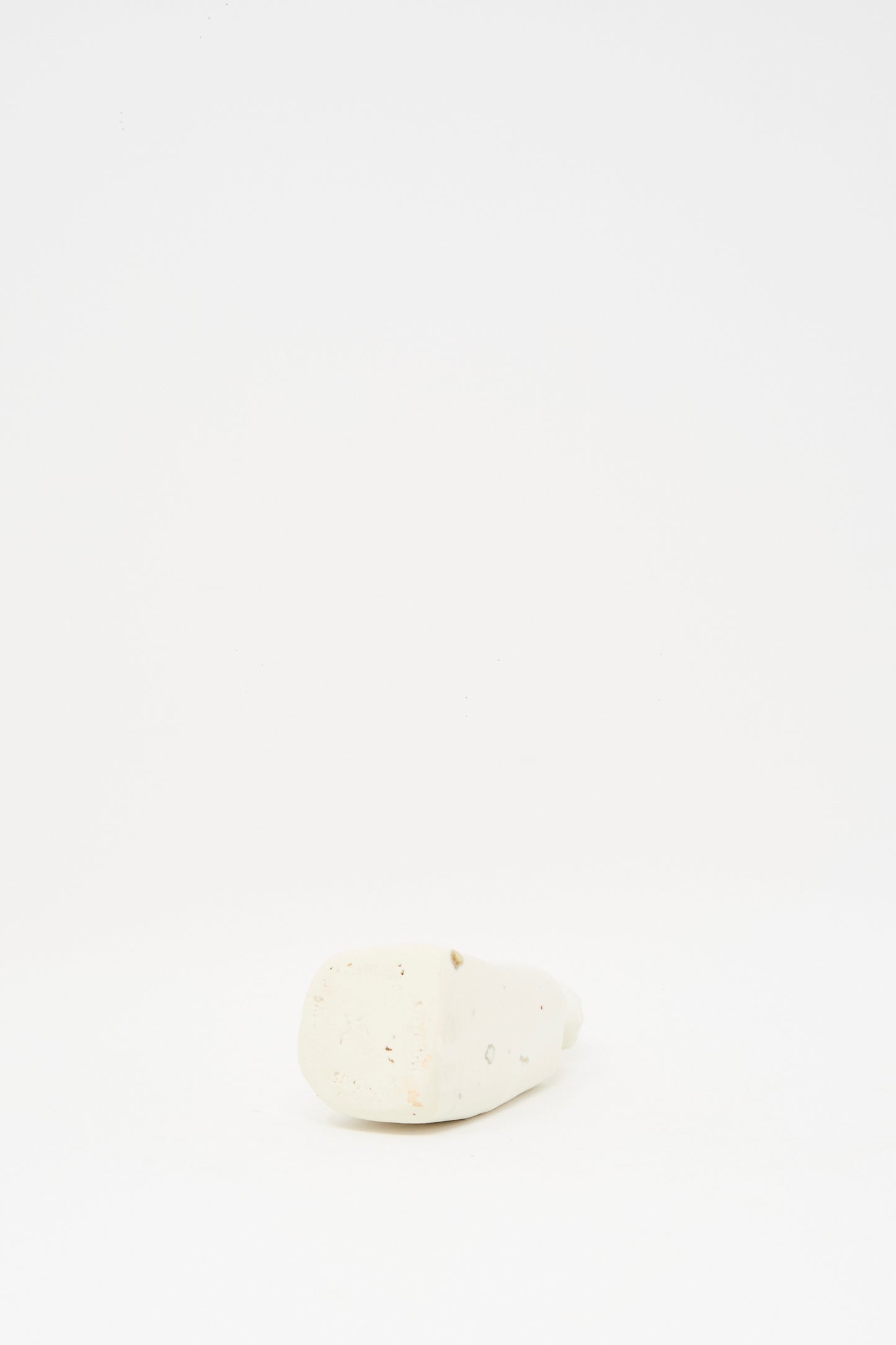 The Carved Bud Vase I by MONDAYS features a small, white, irregular shape and sits on a plain white surface with a white background.