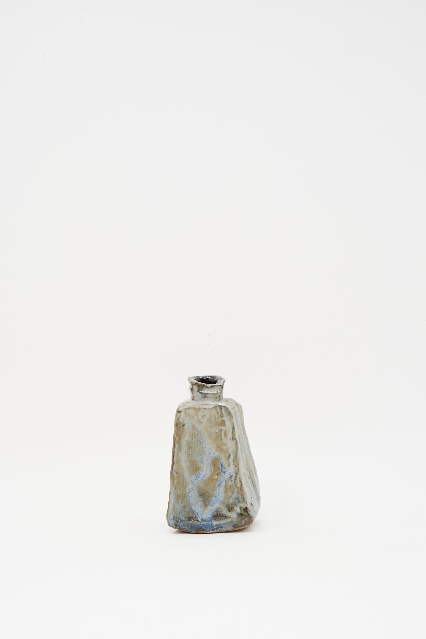 The Carved Bud Vase II by MONDAYS is a small, uniquely shaped clay bud vase with a narrow neck and an earthy blue-brown glaze, carefully crafted in Brooklyn. Set against a plain white background.