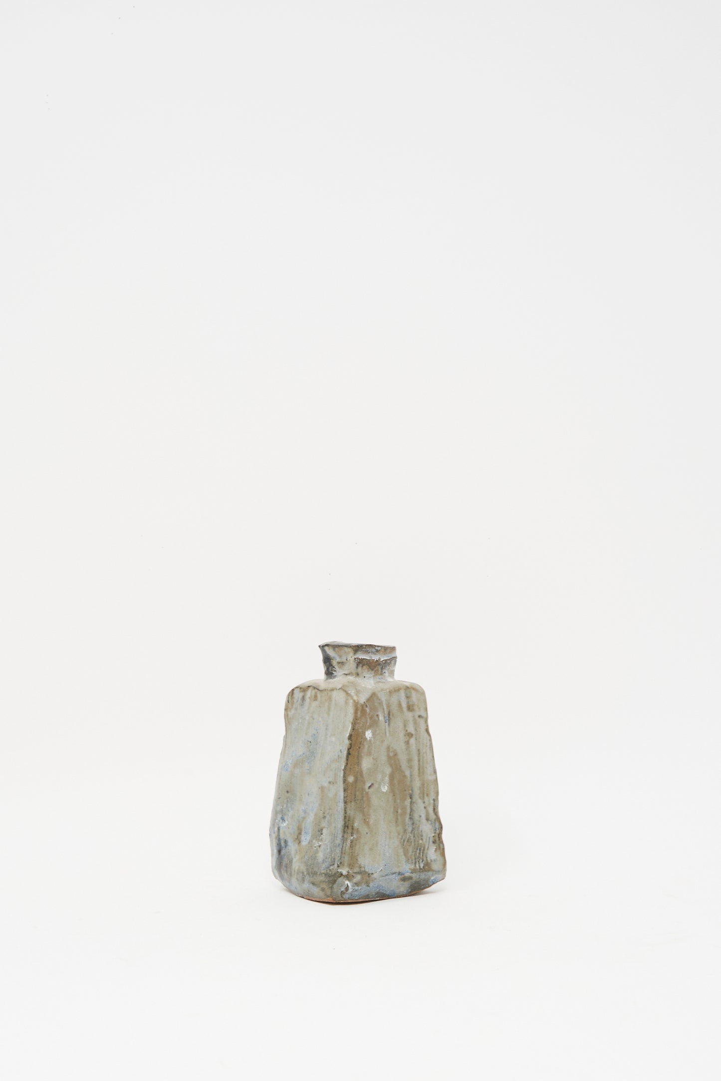 The MONDAYS Carved Bud Vase II is a small, handmade clay vase with an irregular shape and rough, textured surface in earthy tones, displayed against a plain white background.