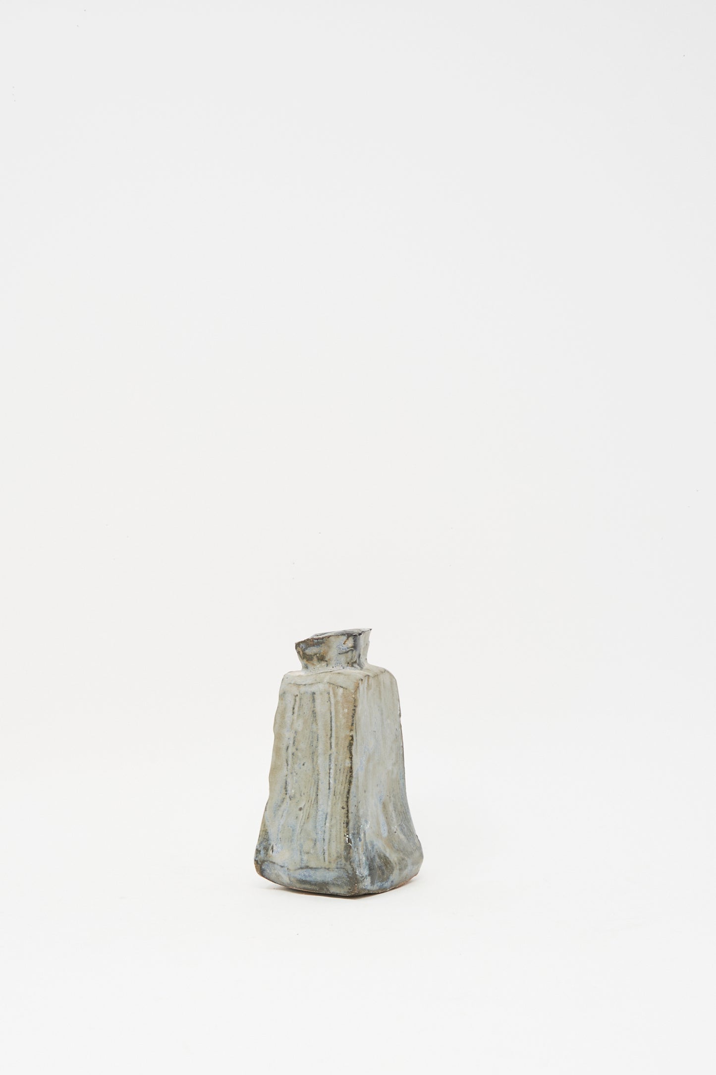 The Carved Bud Vase II by MONDAYS is a small, irregularly shaped clay vase with a narrow, slightly tilted opening, displayed on a white background.