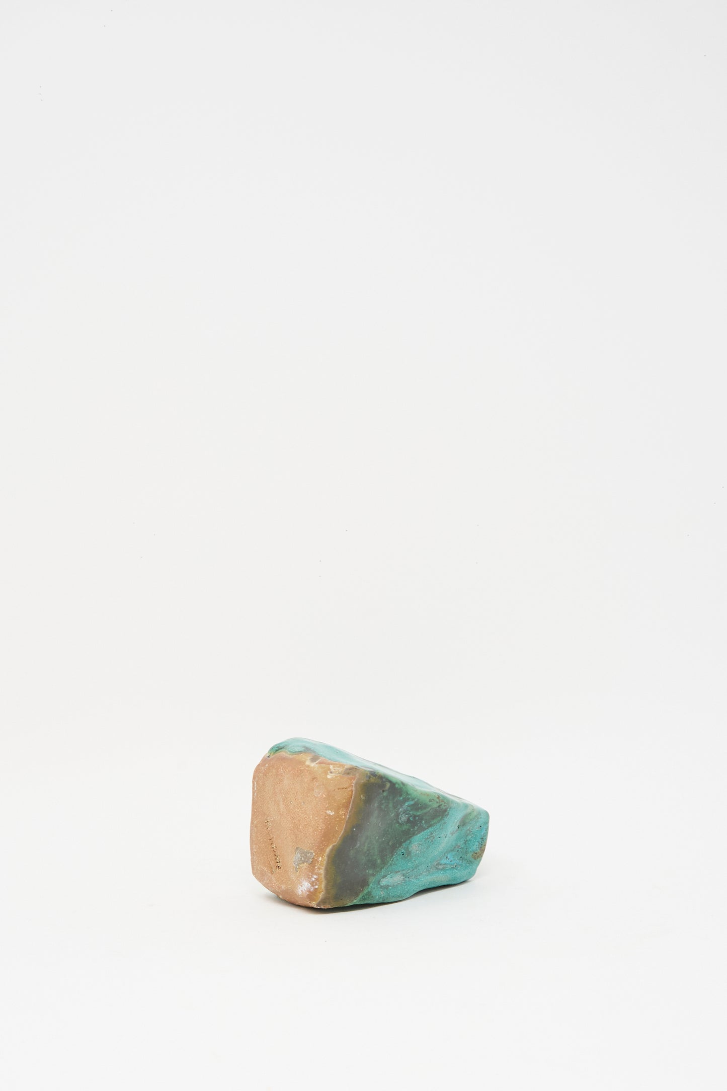 A single Carved Bud Vase III by MONDAYS in turquoise and tan clay sits near the bottom center on a white background, highlighting its handcrafted charm.