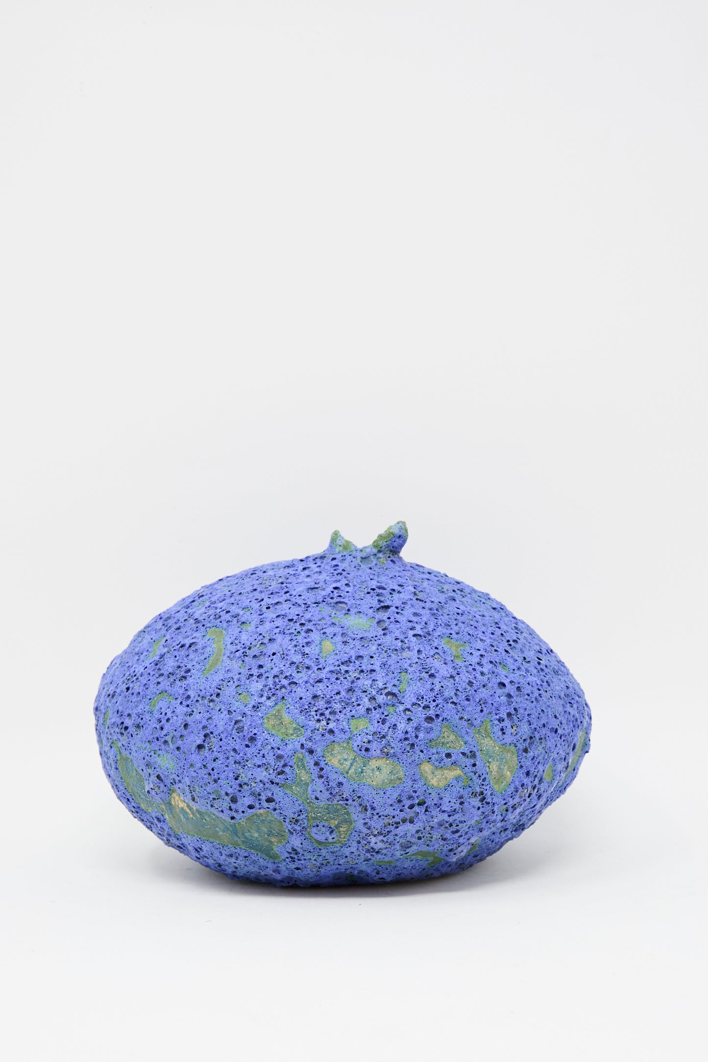 The MONDAYS Glazed Stoneware Moon Vase in Blue, with a round, textured surface and green patches, sits on a plain white background—its lava blue finish highlights its handmade character.