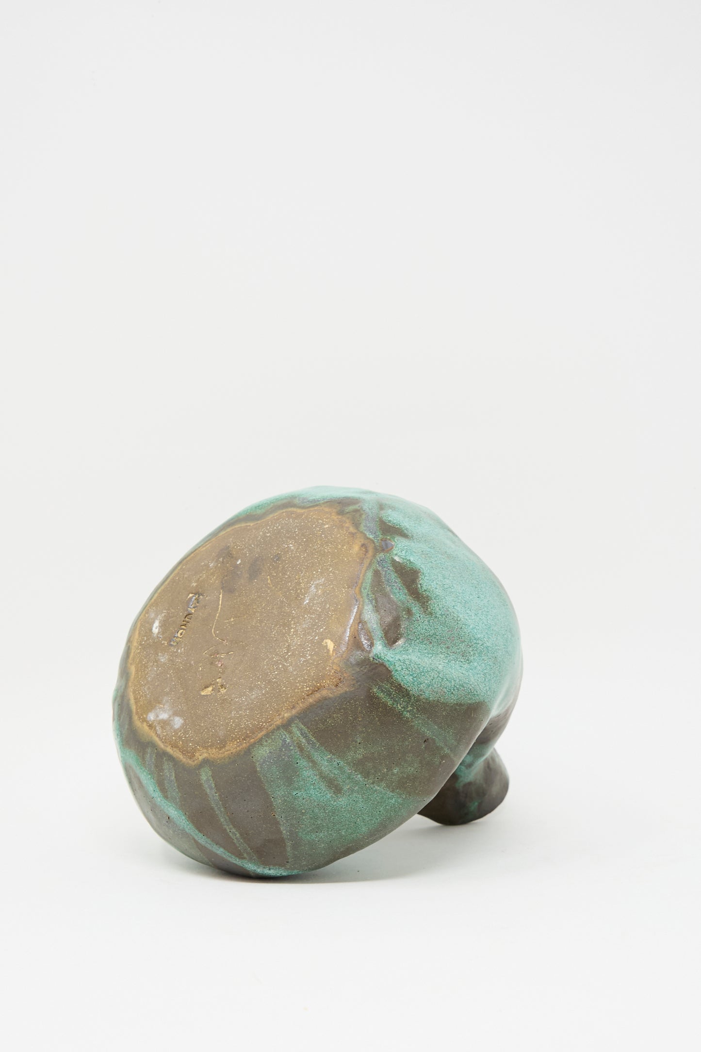 The MONDAYS Glazed Stoneware Pitcher Vase in Green, featuring a round greenish body with a glossy glaze and a flat brown bottom, rests on its side against a plain white background.