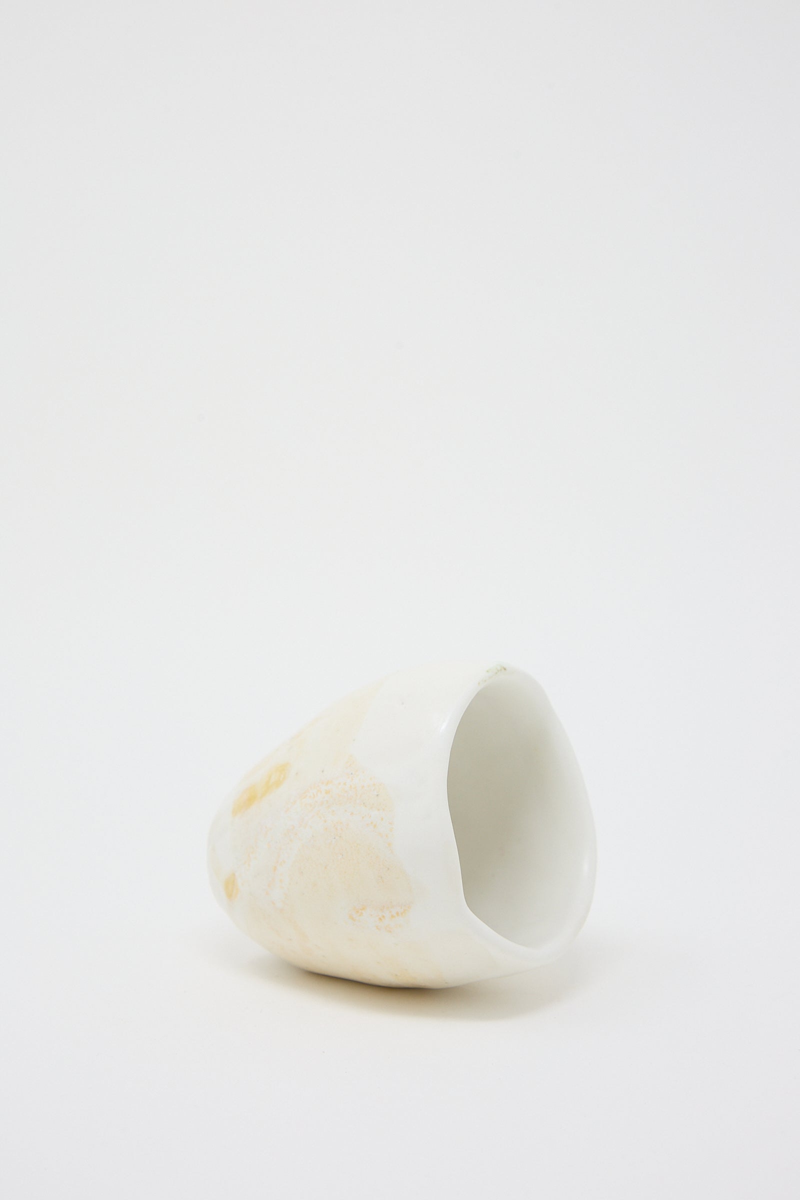 A small beige and white Porcelain Tumbler from MONDAYS on a white surface. Vessel laying on its side.