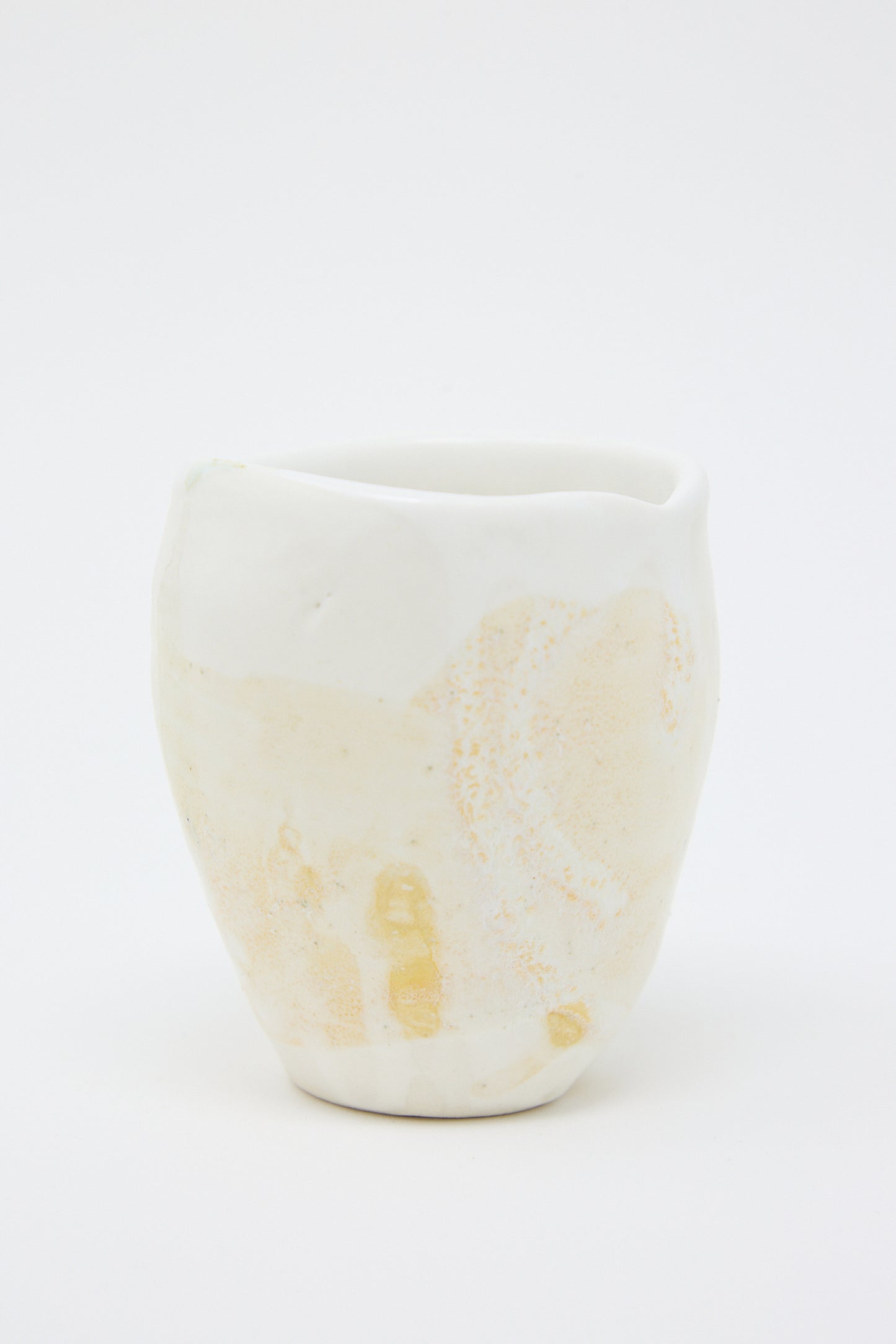 A beige and white porcelain tumbler from MONDAYS with a textured yellow glaze. Up close view.