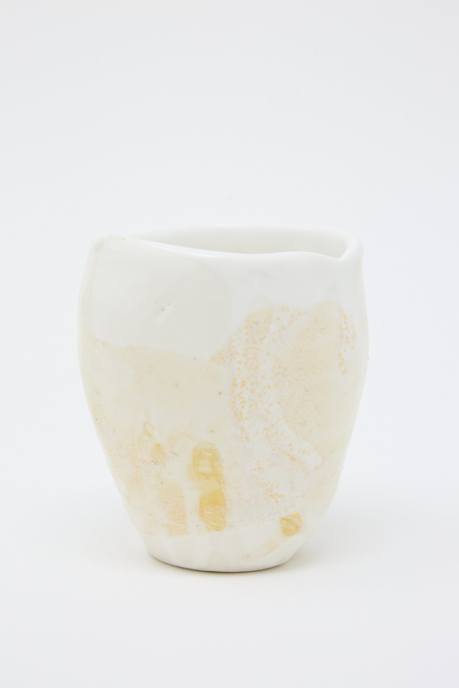 A beige and white porcelain tumbler from MONDAYS with a textured yellow glaze. Up close view.
