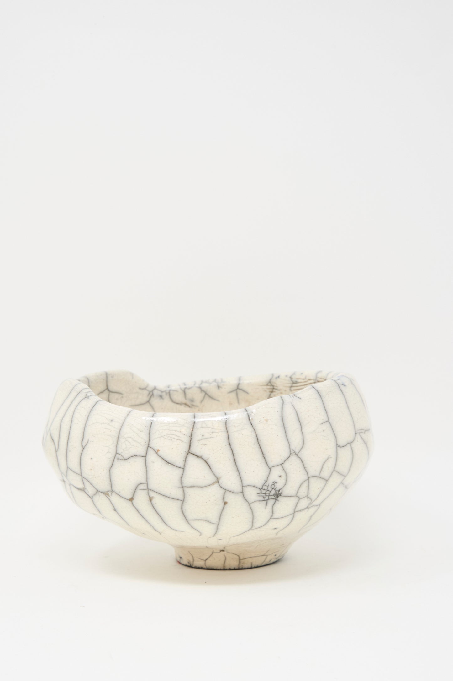 The MONDAYS Raku Coiled Bowl is a white ceramic piece with a rounded shape and a unique crackle glaze, shown against a plain white background.