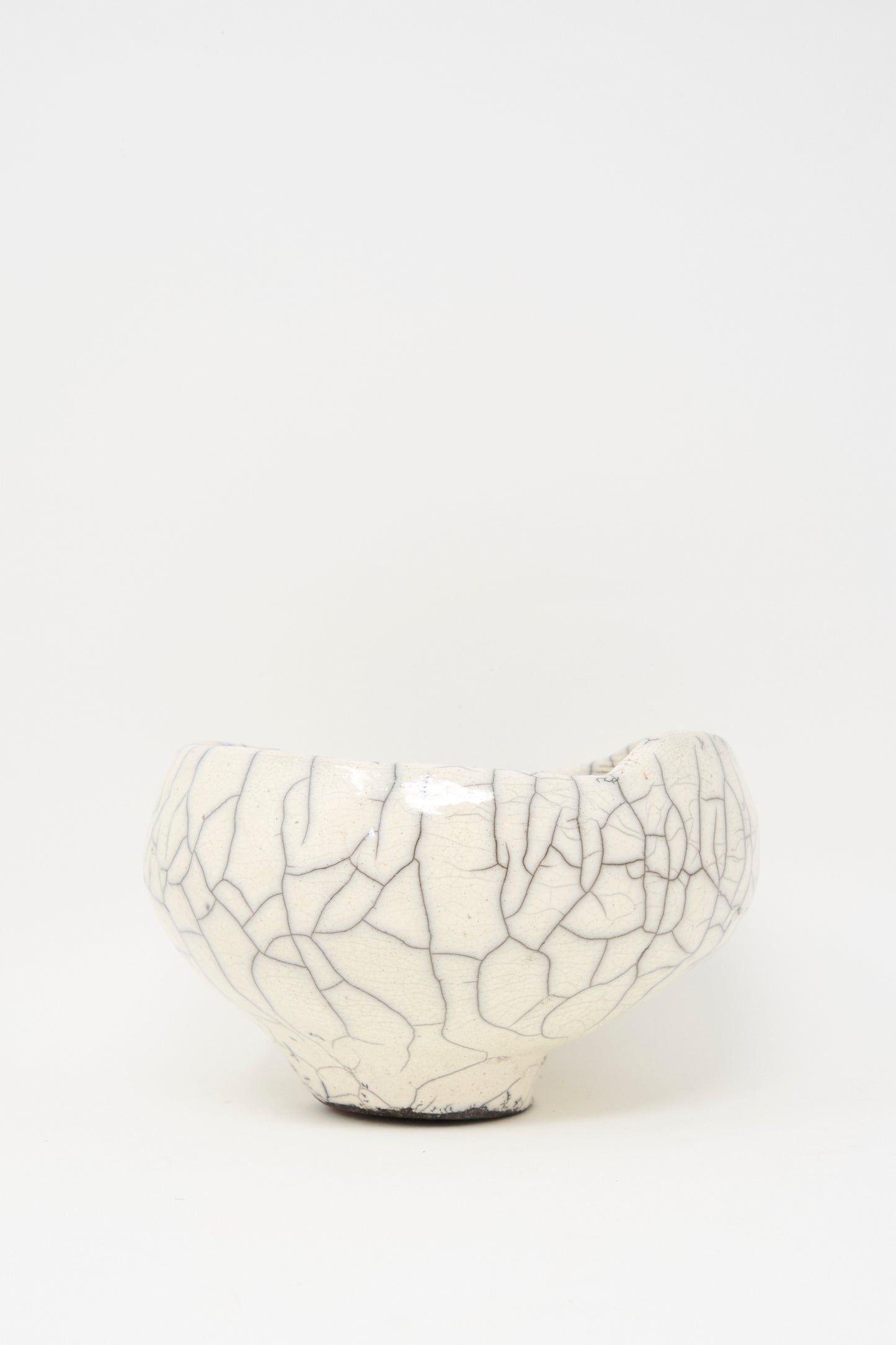 The MONDAYS Raku Coiled Bowl is a round, white ceramic piece with a unique crackle glaze, crafted in Raku-fired stoneware and displayed against a plain white background.