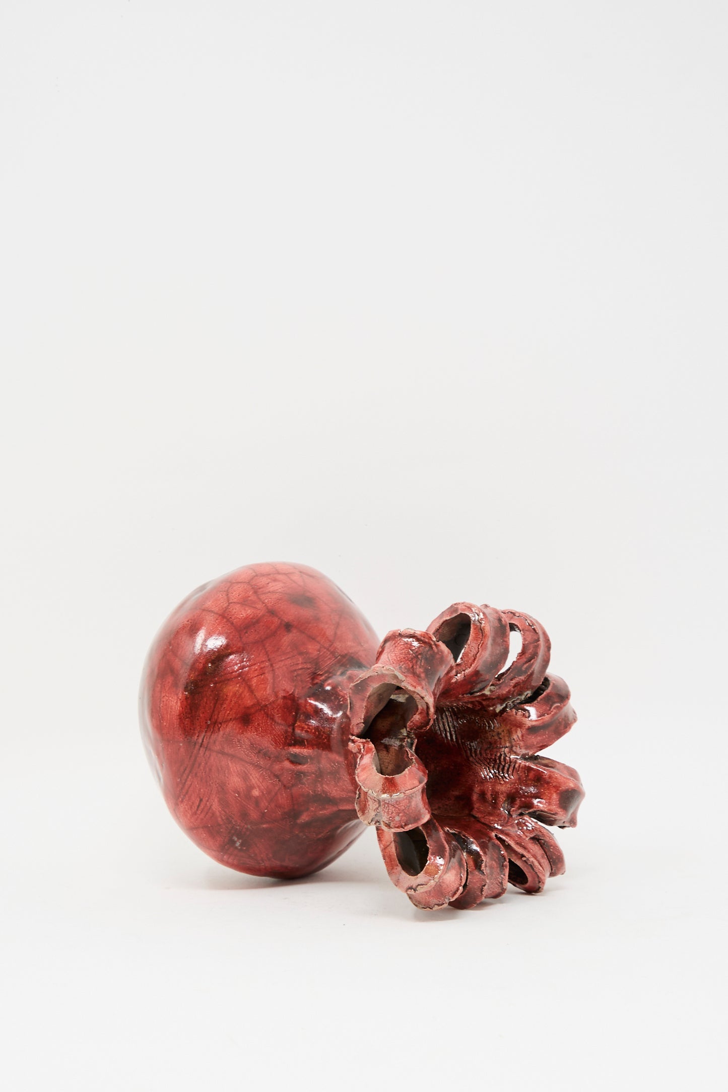 The MONDAYS Raku Ribbon Vase in Red, a glossy sculptural piece inspired by a pomegranate, lies on its side against a plain white background.