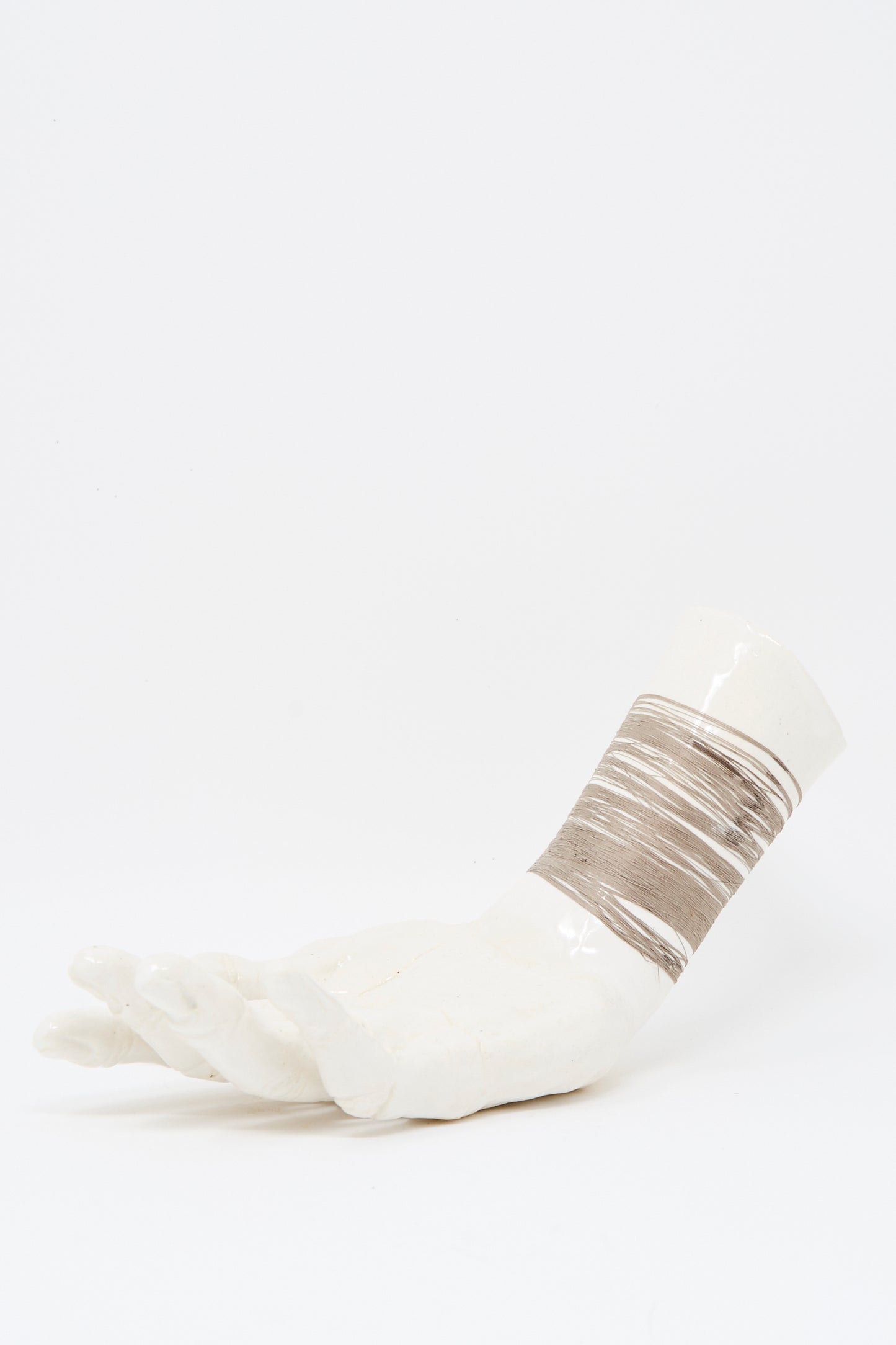 The Monty J Ceramic Hand Sculpture with Grey Thread features a white ceramic hand resting on its side, accented by grey thread wrapped around the wrist.
