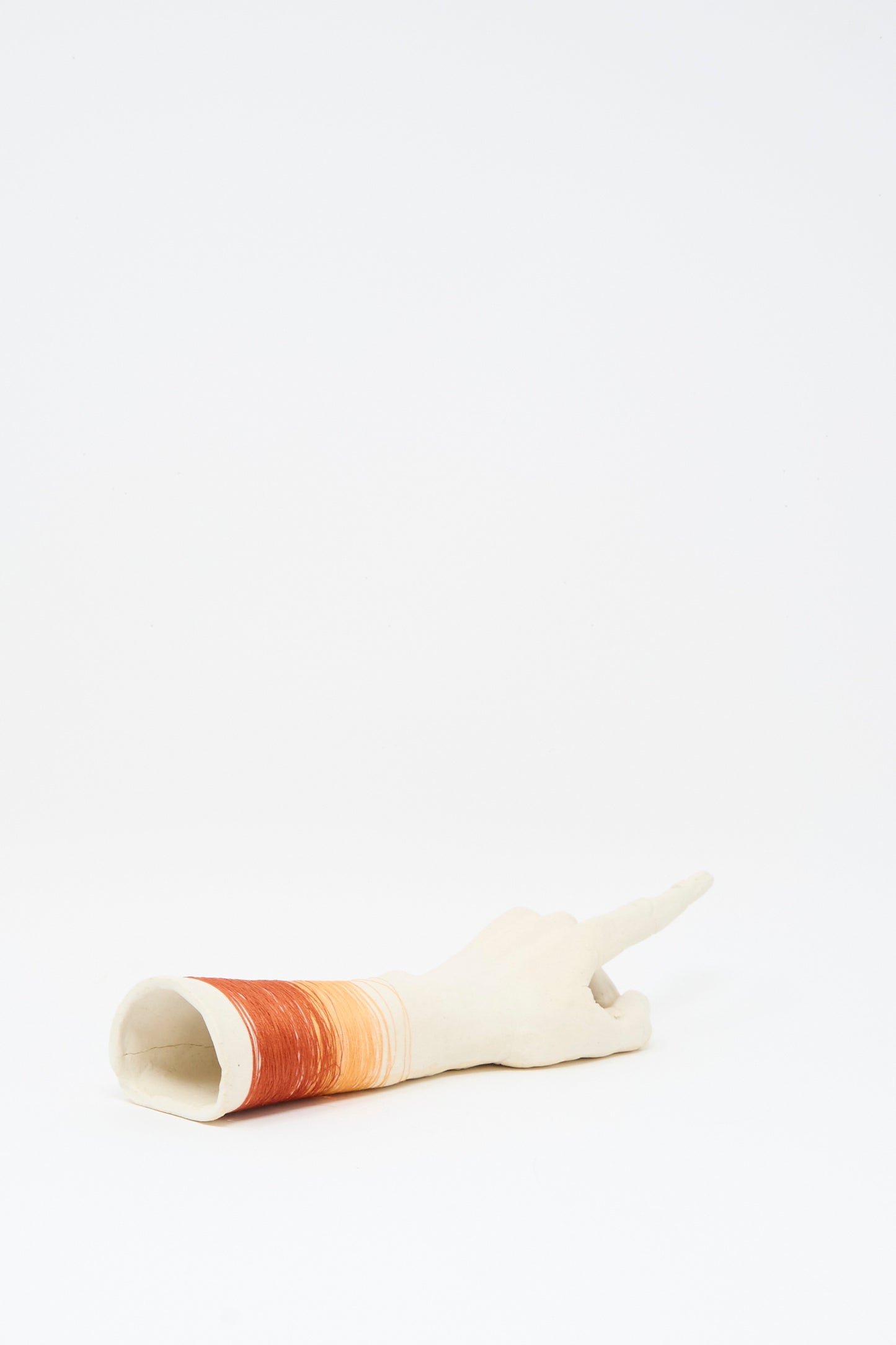 The Monty J Ceramic Hand Sculpture with Orange and Red Thread, handmade in Brooklyn, features a human hand with an extended index finger and colorful thread accents, displayed on a plain white surface.