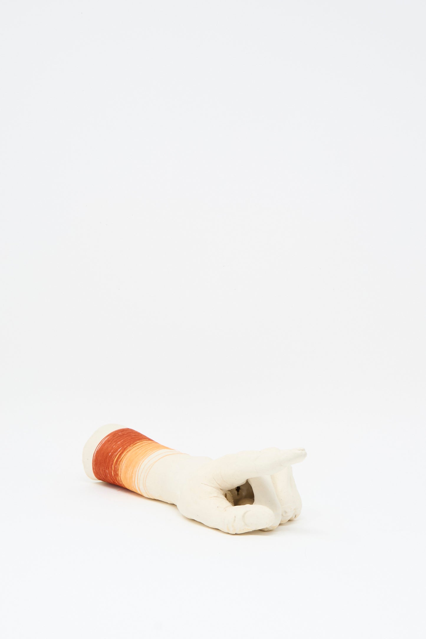 The Monty J Ceramic Hand Sculpture with Orange and Red Thread rests on a white surface, its index finger pointing outward.