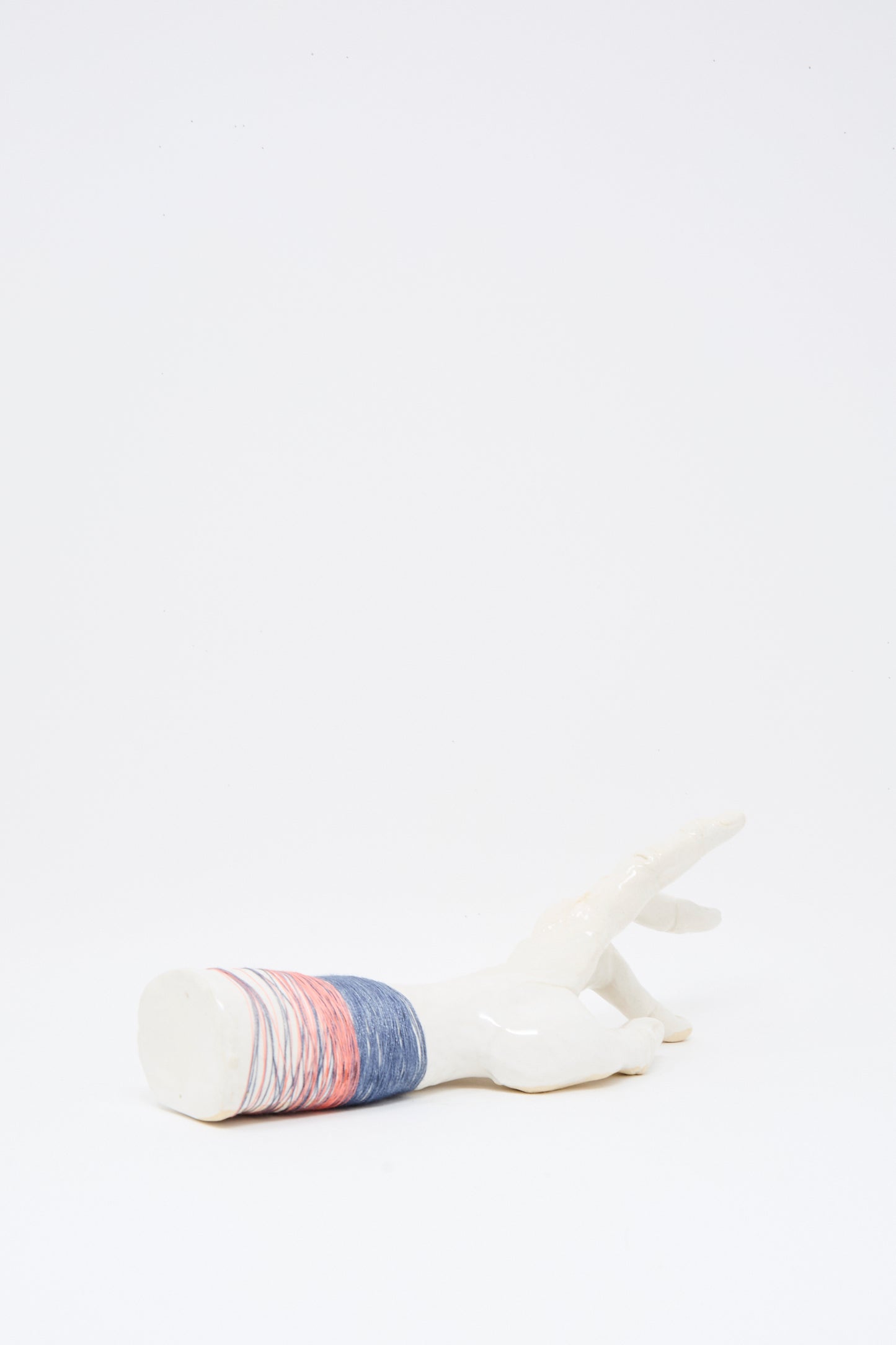 The Monty J Ceramic Hand Sculpture with Pink and Blue Thread, handmade in Brooklyn, features horizontal blue, pink, and red bands around the wrist on a white ceramic base.
