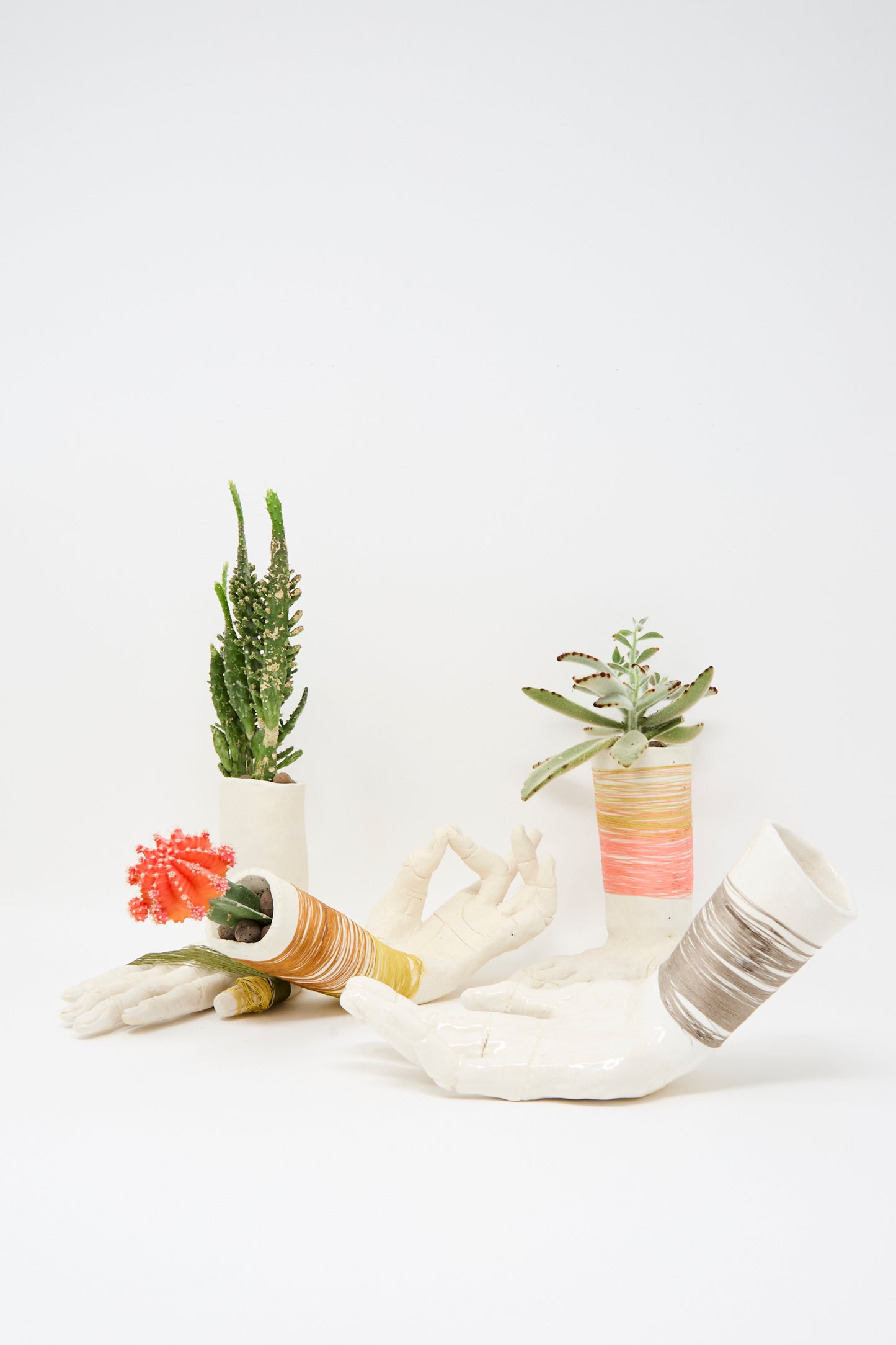 The Monty J Ceramic Hand Sculpture with Pink and Gold Thread holds small succulents and cactus, displayed against a plain white background.