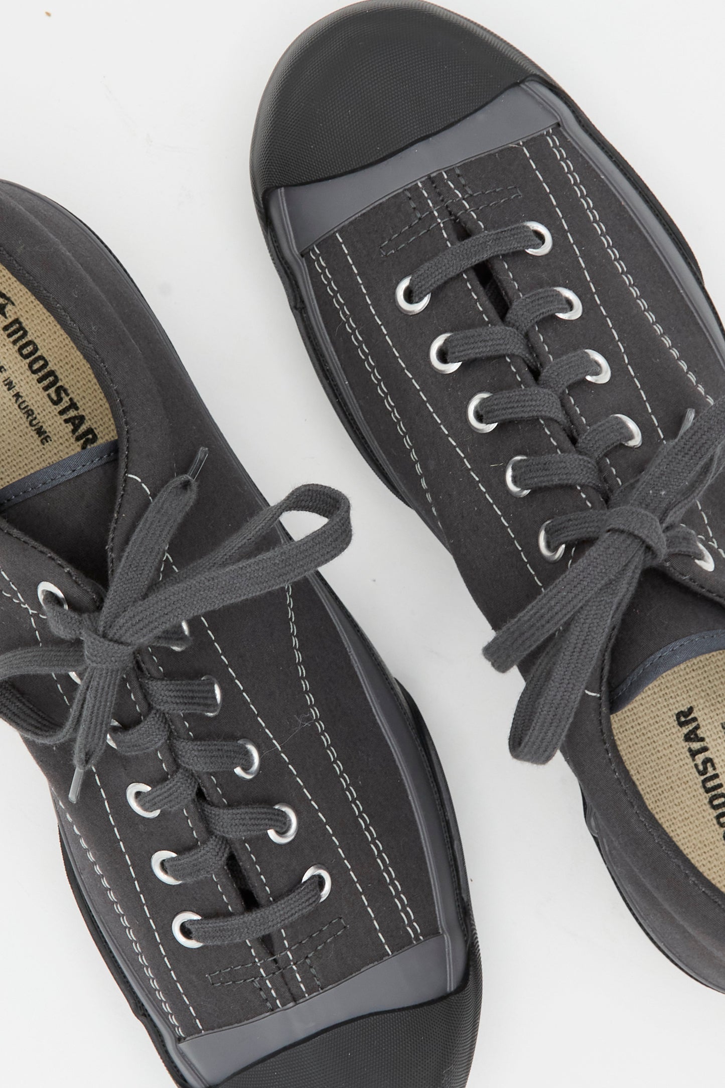 The Gym Court Sneaker in Charcoal by Moonstar features black cotton nylon canvas, gray rubber toe caps, white stitching, laces, and visible brand labels on the insoles.