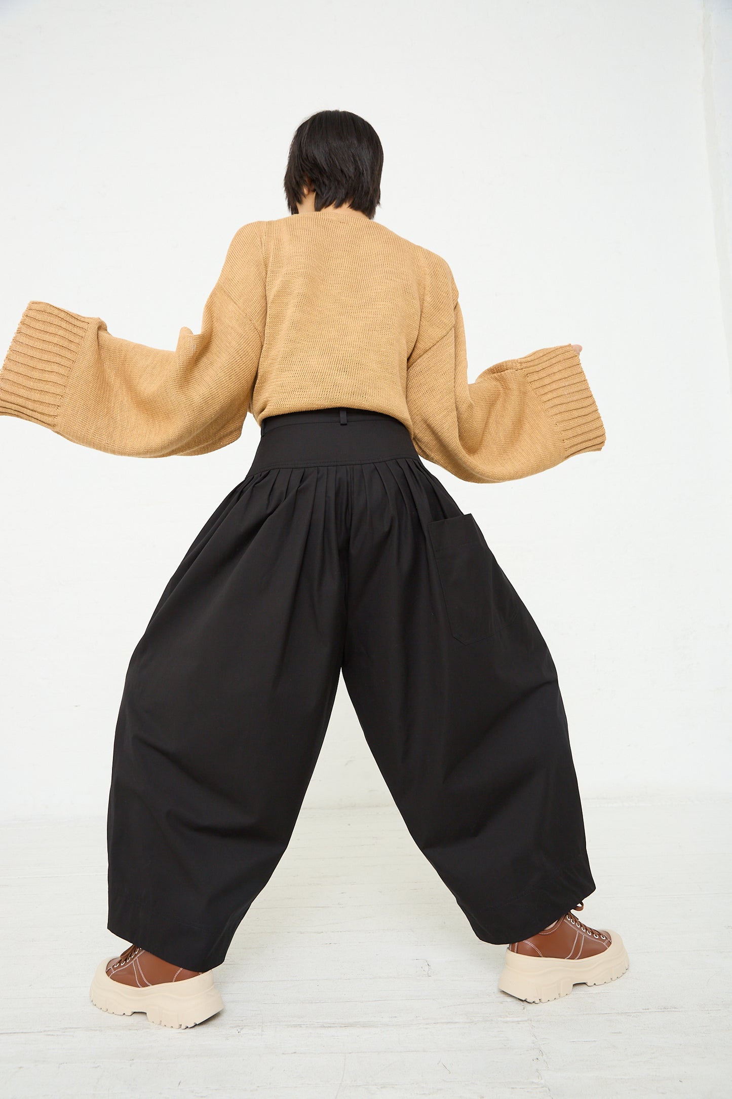 A woman in Niccolò Pasqualetti's Cotton Twill Luna Trouser in Black and a beige sweater. Back view.