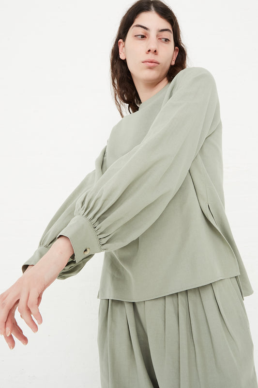 The model is wearing a Cotton Twill Puff Sleeve Blouse in Agave by Black Crane with pleated pants.