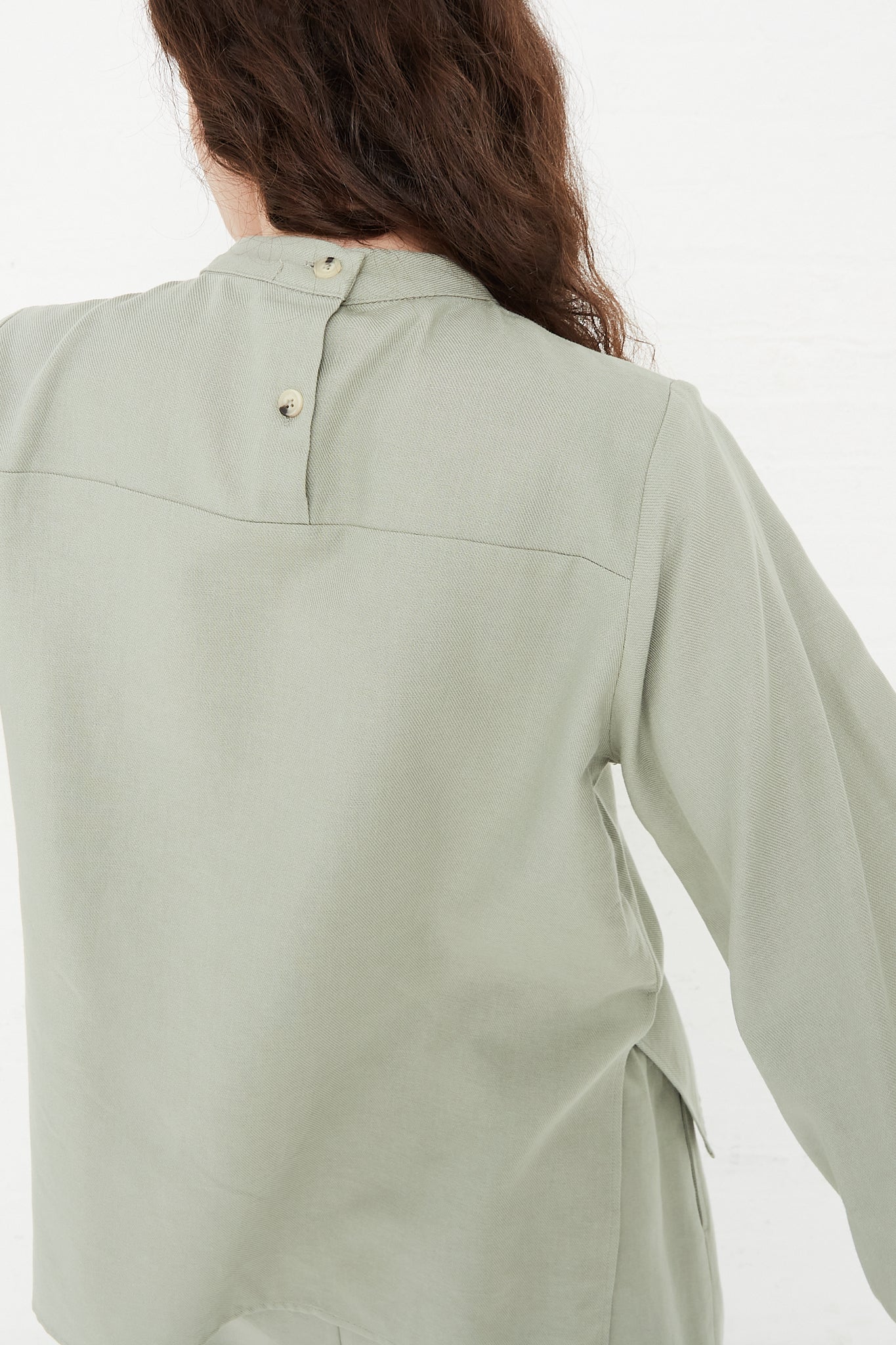 The back view of a woman wearing a Black Crane Cotton Twill Puff Sleeve Blouse in Agave. Up close view of back details.
