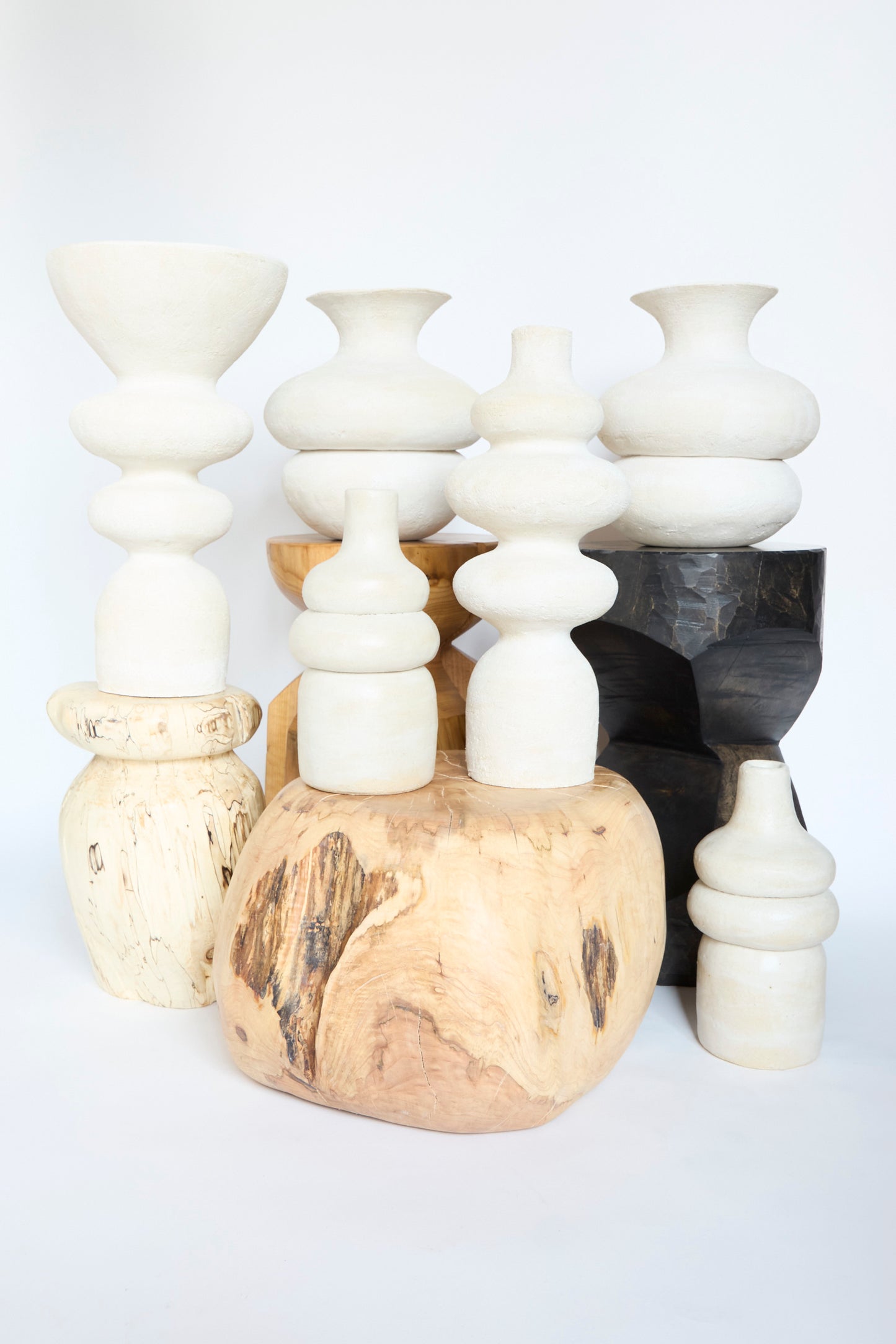The Monolith Vessel by Oatmeal is featured alongside other abstract, handmade ceramic pieces in various shapes and neutral tones, stacked against a plain backdrop.
