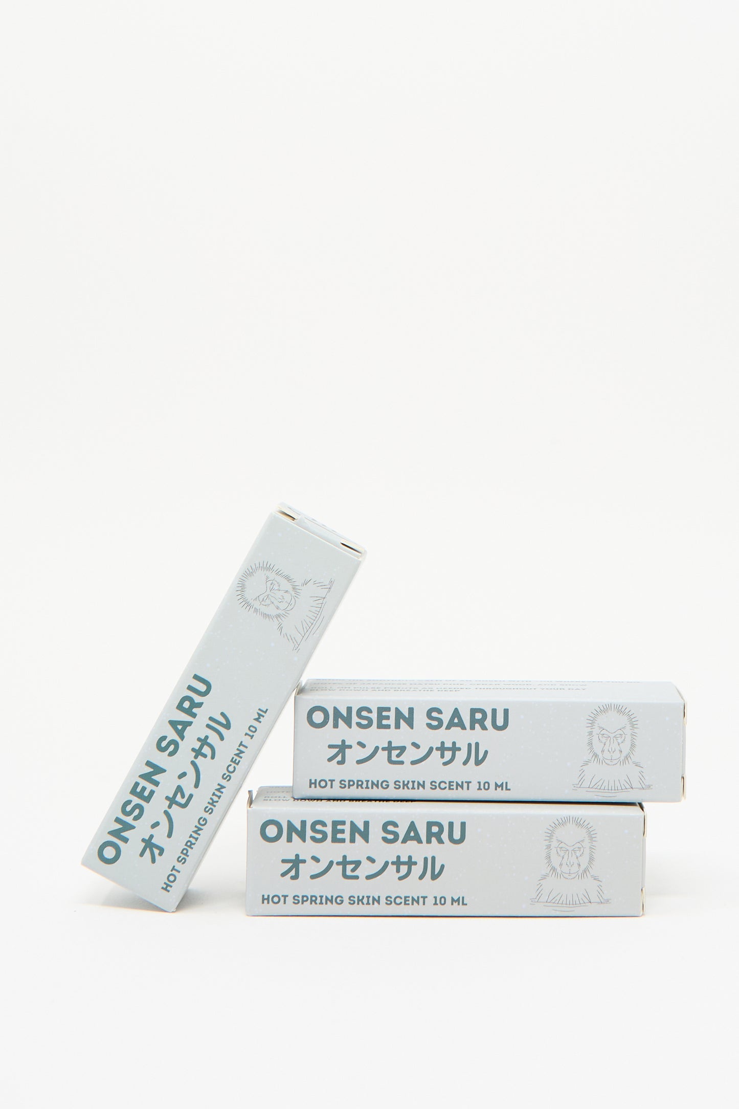 Three boxes of Onsen Saru's Hot Spring Skin Scent, each containing 10 ml, showcase minimalist packaging adorned with Japanese text and a monkey illustration. This natural perfume embodies the essence of a Japanese Matsu pine, delivering a refreshing unisex fragrance.
