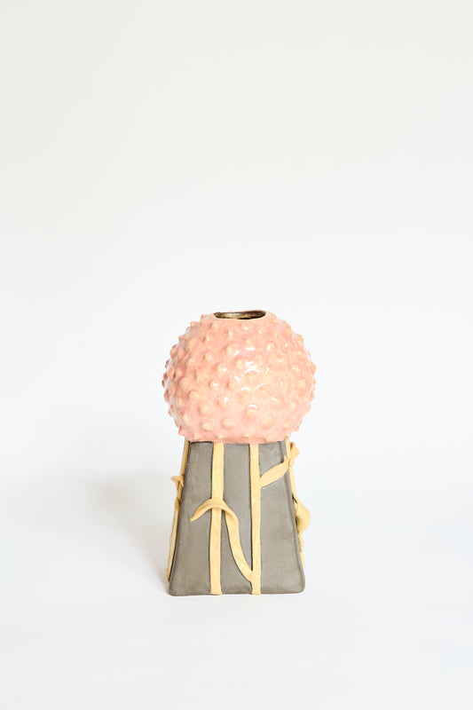 The Allium Vase Small by Pearce Williams is a handmade stoneware piece from New Orleans, featuring a pink textured spherical top, gray angular base with yellow ribbon accents, and displayed on a plain white background.