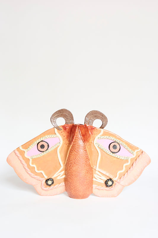 The Emperor Moth in Rust by Pearce Williams is a glazed stoneware sculpture featuring large orange and pink wings, black and white circular patterns, and textured brown antennae, displayed on a plain white background.