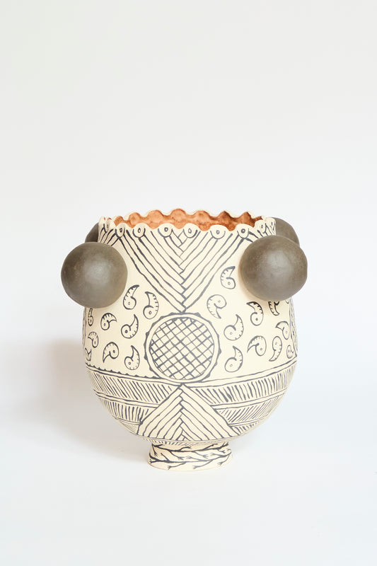 The Pearce Williams Patterned Round Urn is a handmade stoneware piece with black geometric and paisley designs, two round gray side protrusions, and a scalloped rim, shown on a plain white background.