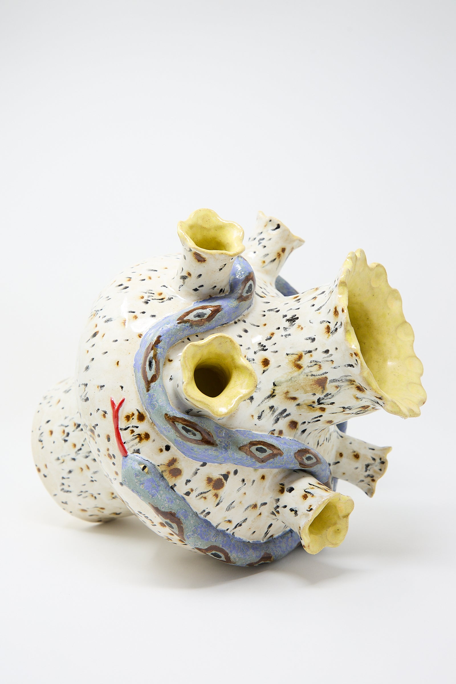 A ceramic sculpture of a whimsical, abstract creature with multiple openings and colorful patterns on a white background, crafted from glazed stoneware, by Pearce Williams.