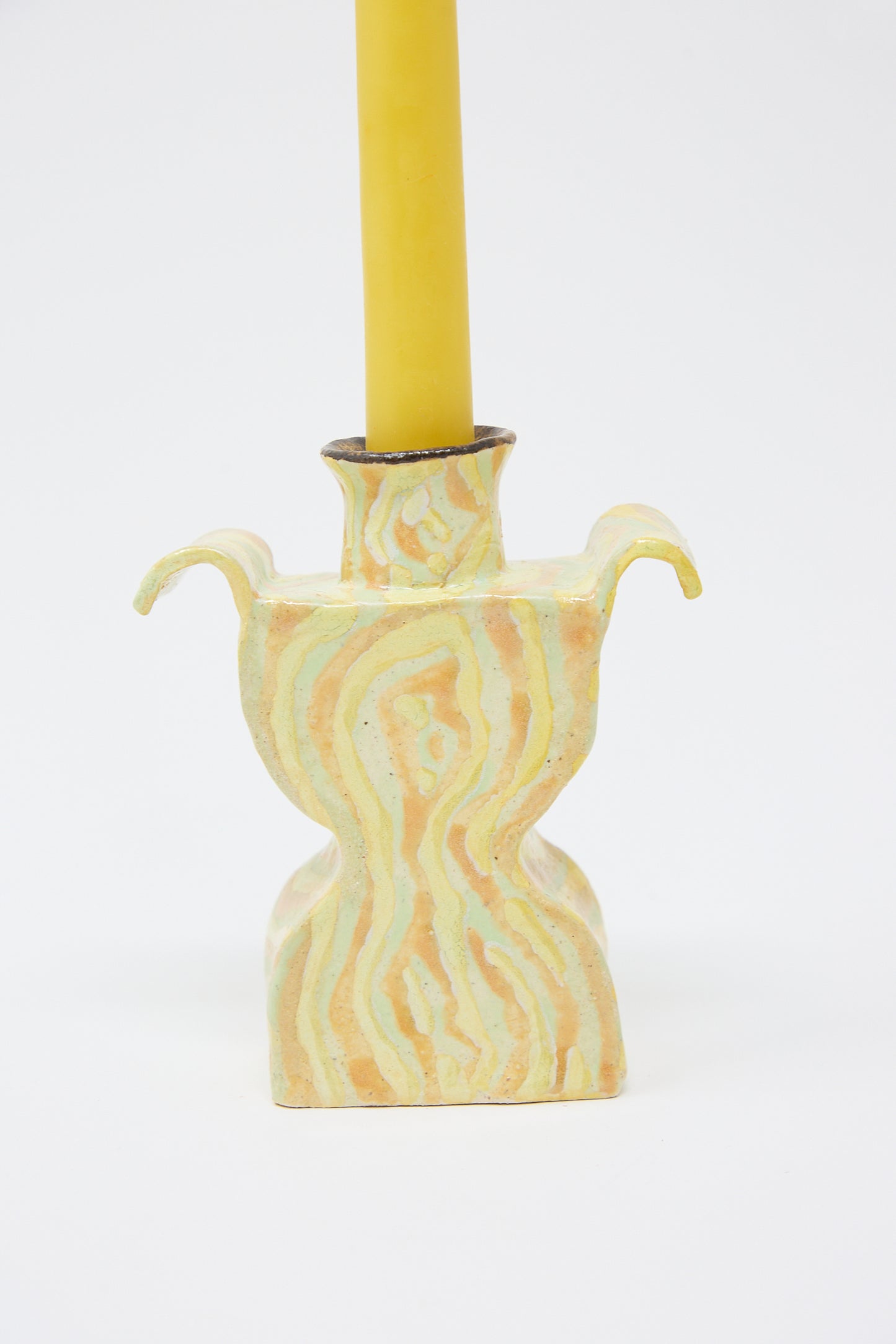 A handcrafted ceramic Woodgrain Candlesticks Pair with a swirling yellow and white pattern, featuring two curved handles, supporting a yellow candle by Pearce Williams.