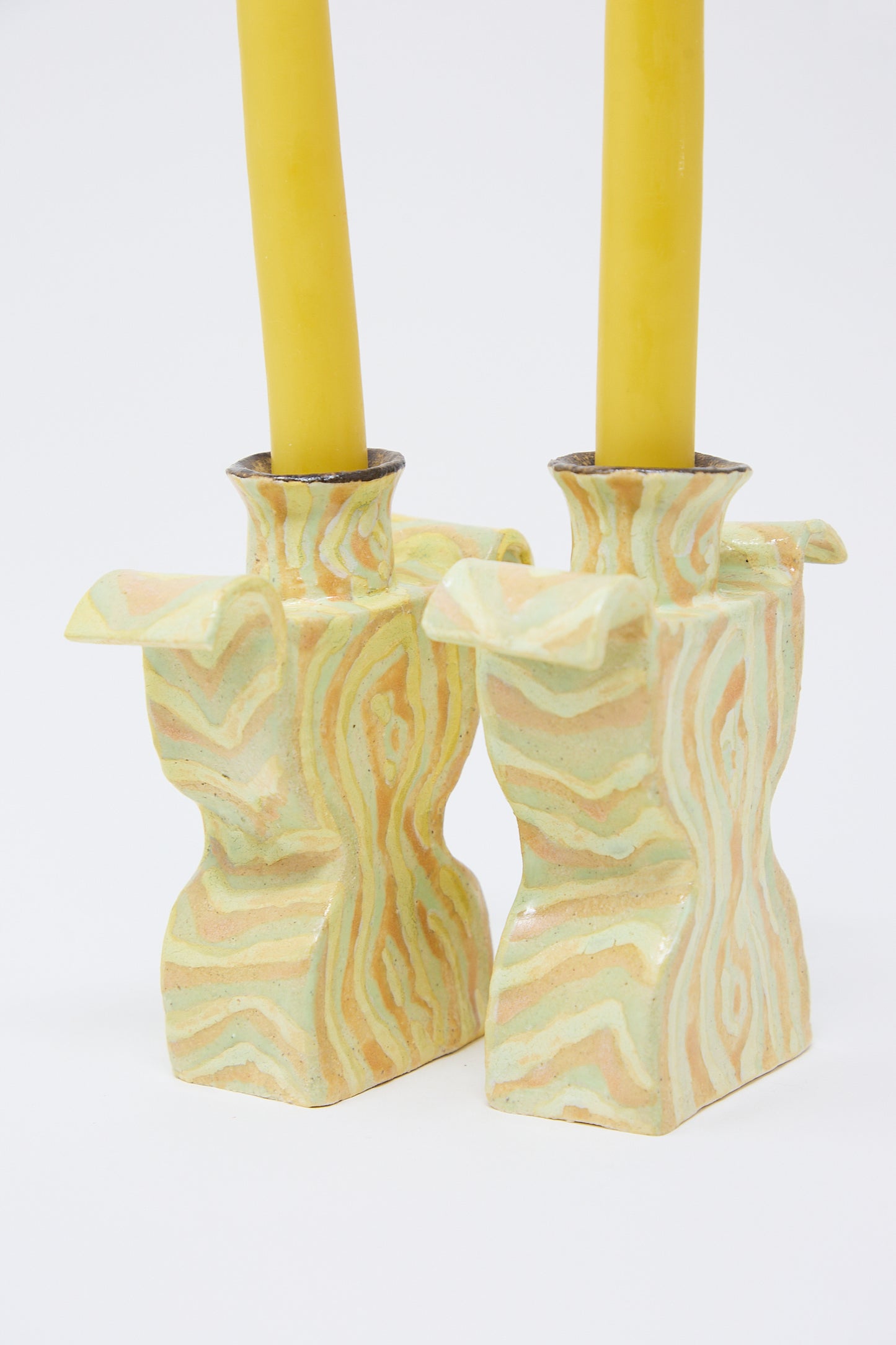 Two yellow candles standing in matching Pearce Williams Woodgrain Candlesticks Pair on a white background.
