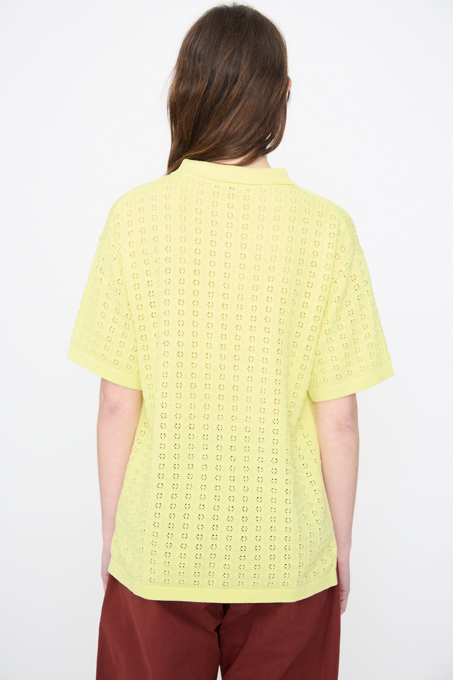 A person with long brown hair is shown from the back, wearing the Rachel Comey Clarence Polo in Limoncello and maroon pants, against a plain white background.