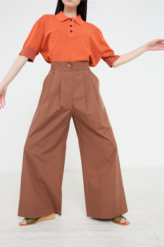 A person in a bright orange top and wide-leg, high-waisted brown Rachel Comey Coxsone Pant in Sienna standing against a white background.