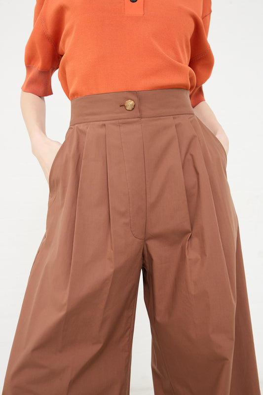 A person wearing a rust orange top tucked into high-waisted brown pleated Rachel Comey Coxsone Pant in Sienna trousers.