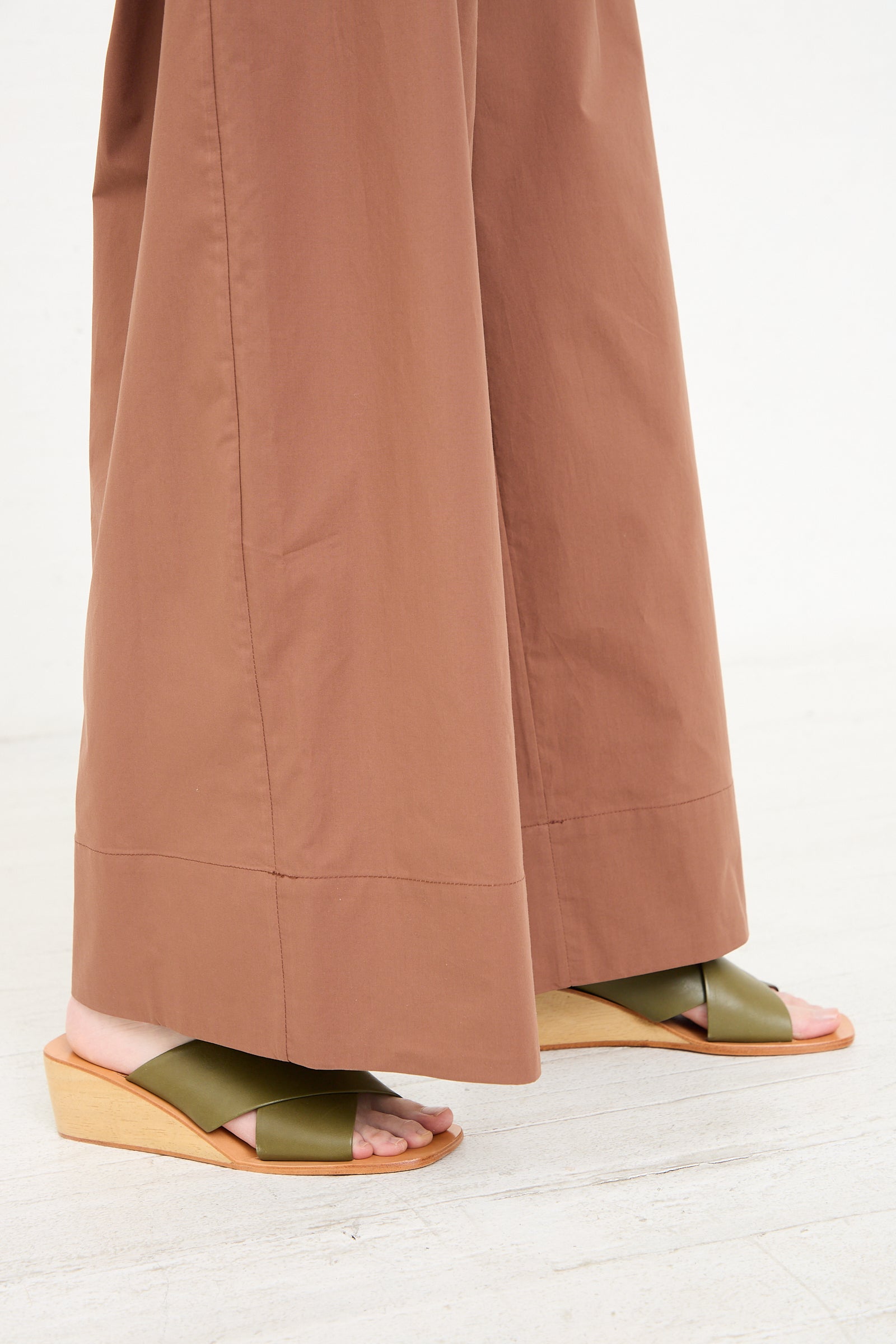 A person wearing the Rachel Comey Coxsone Pant in Sienna and green open-toed sandals with wooden heels.