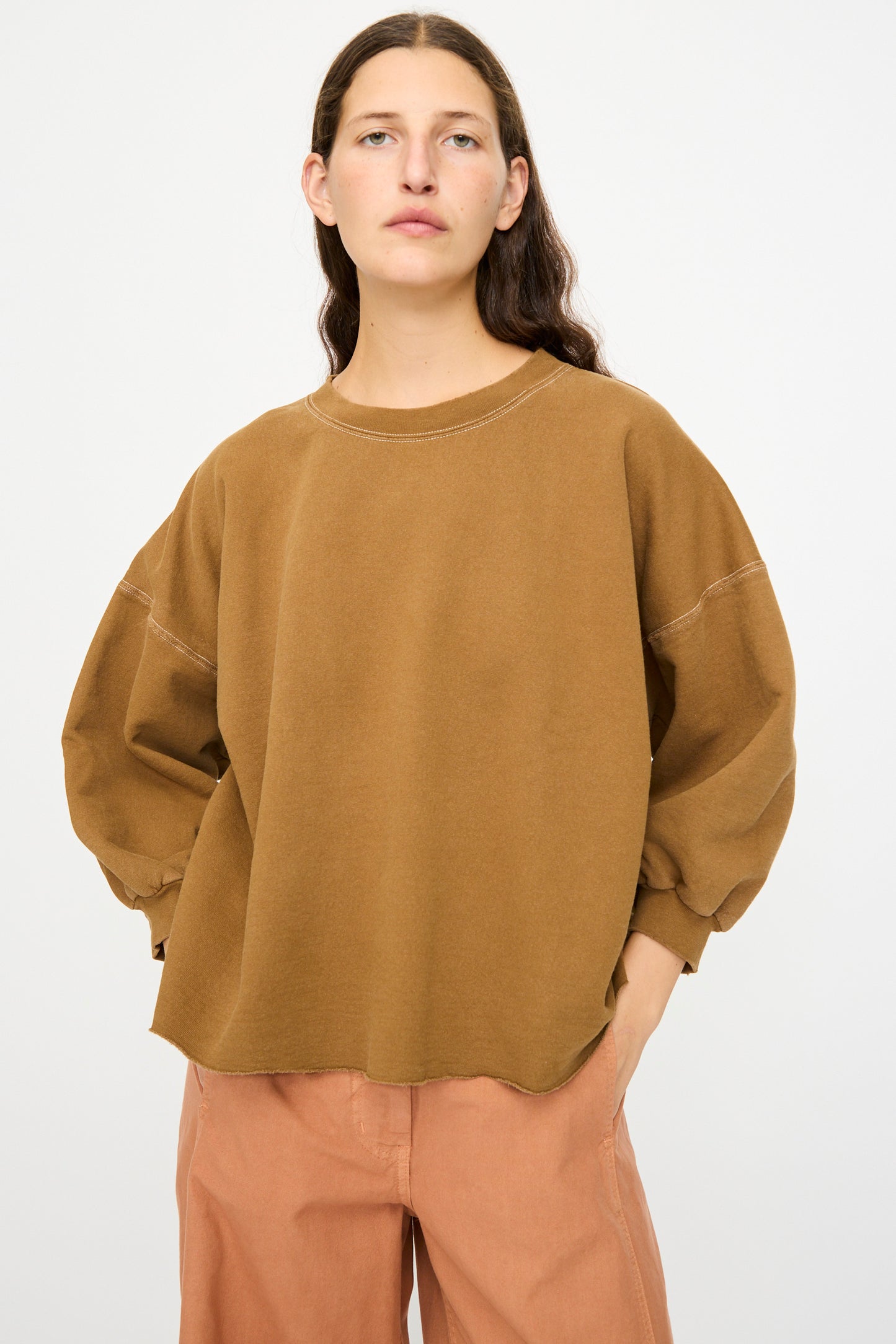 Model wears the Rachel Comey Fond Sweatshirt in Bronze—an oversized, distressed cotton long-sleeve top—paired with light brown pants, standing against a plain white background.