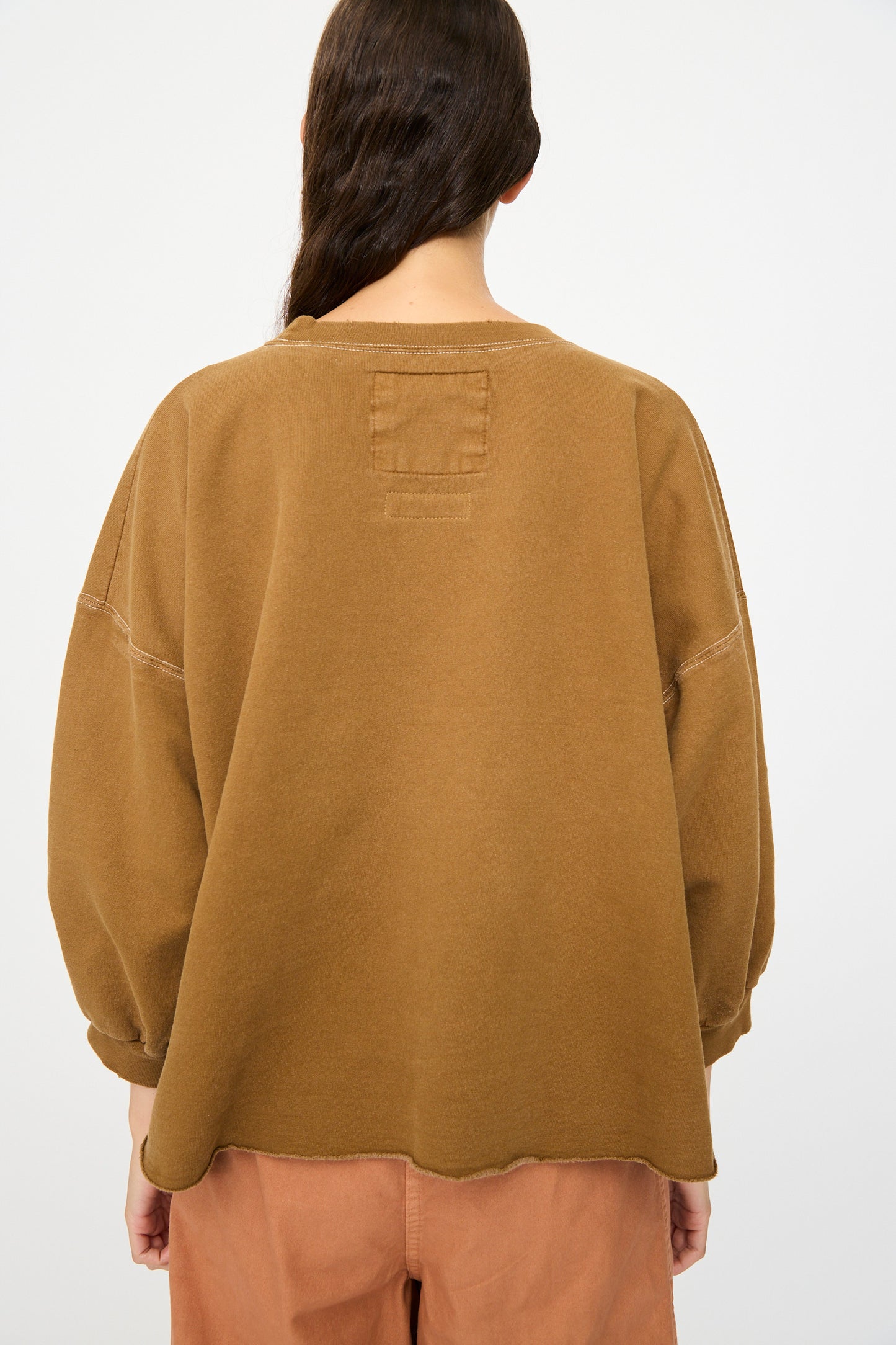 A person stands with their back to the camera, wearing the Rachel Comey Fond Sweatshirt in Bronze and light brown pants for a relaxed, effortless look.