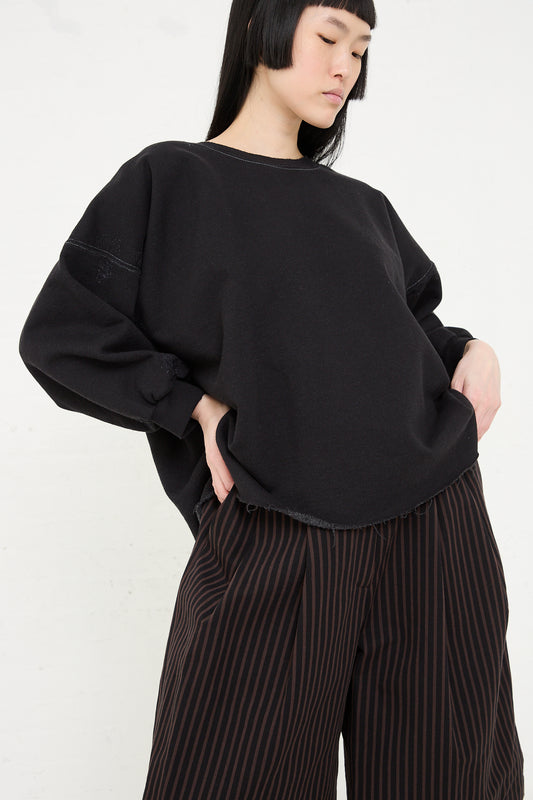 Woman in a black Rachel Comey Fond Sweatshirt in Charcoal and striped trousers posing against a white background.