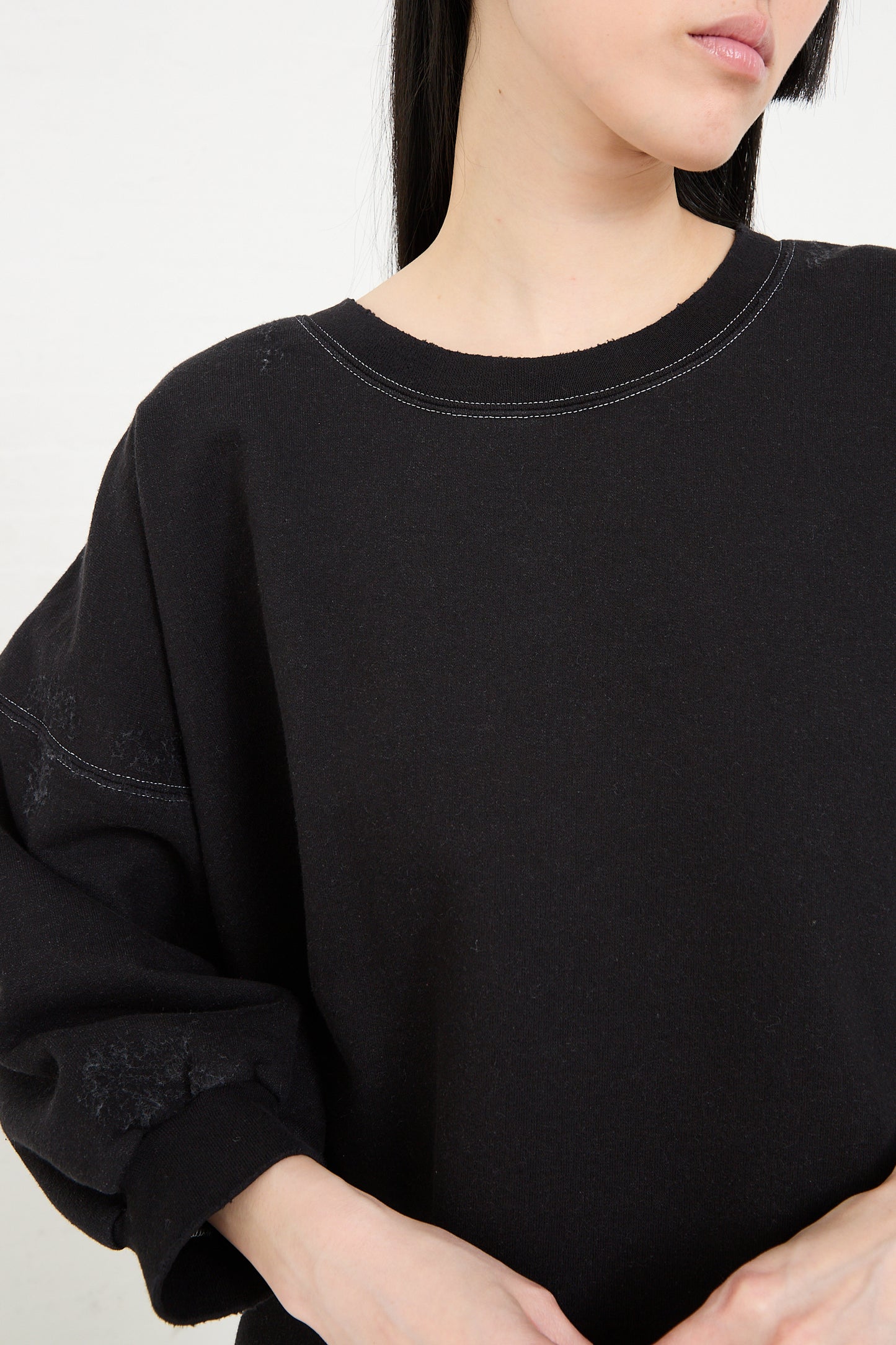 A person wearing a Rachel Comey Fond Sweatshirt in Charcoal, a plain black, genderless oversized sweatshirt with a round neck, with a partial view of their profile.